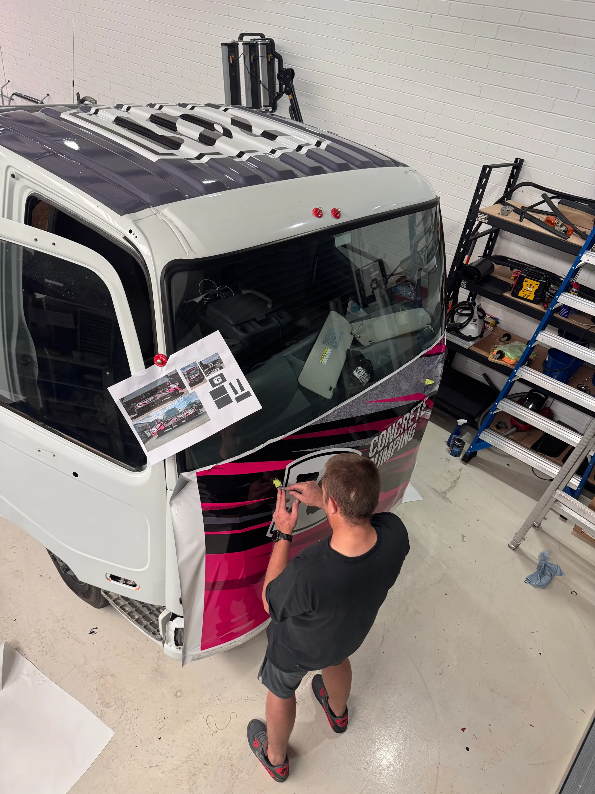 Installer seen from behind fitting 701 Concrete Pumping graphics to a truck cab