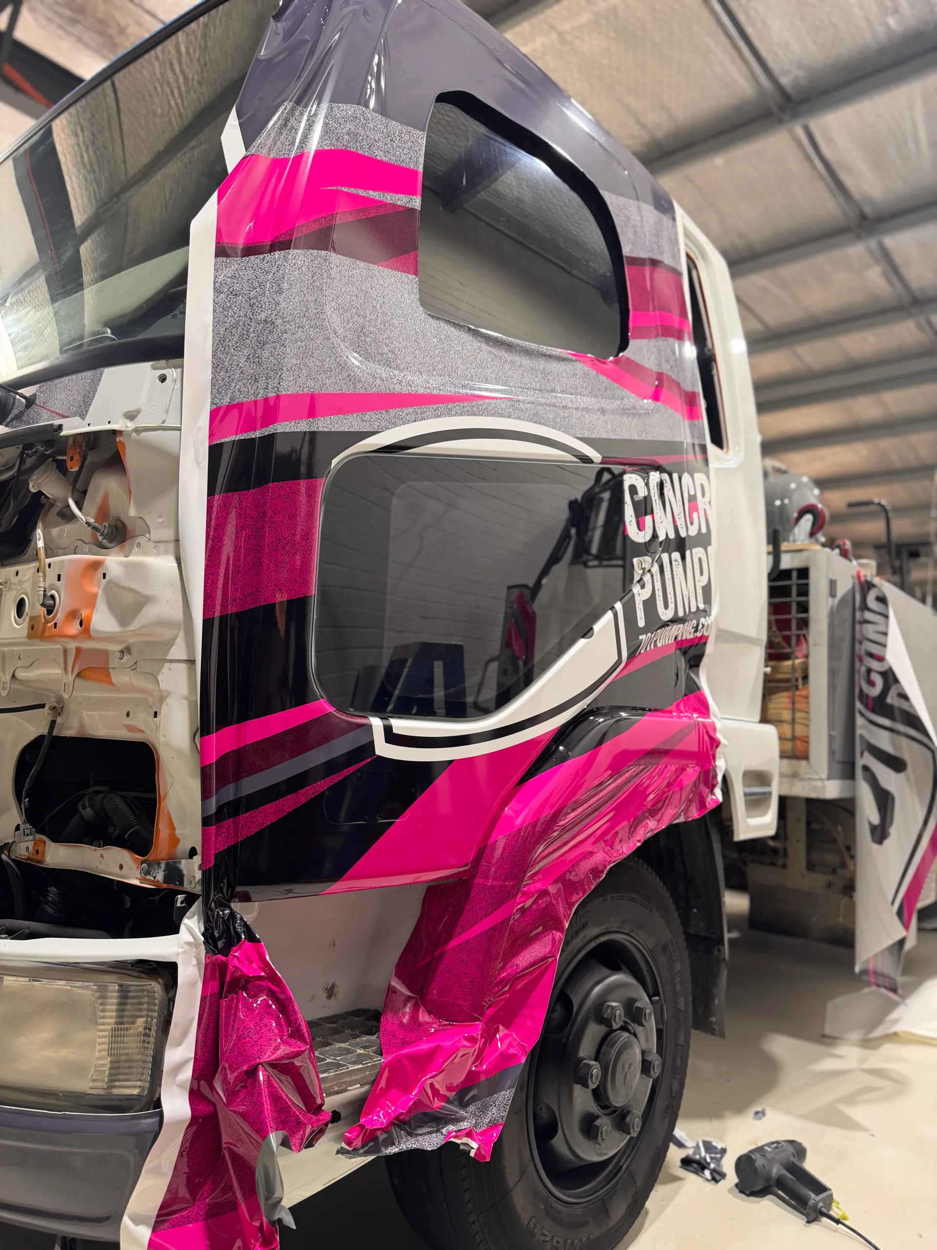 Loose pink and grey film around the truck cab wheel arch during graphics installation