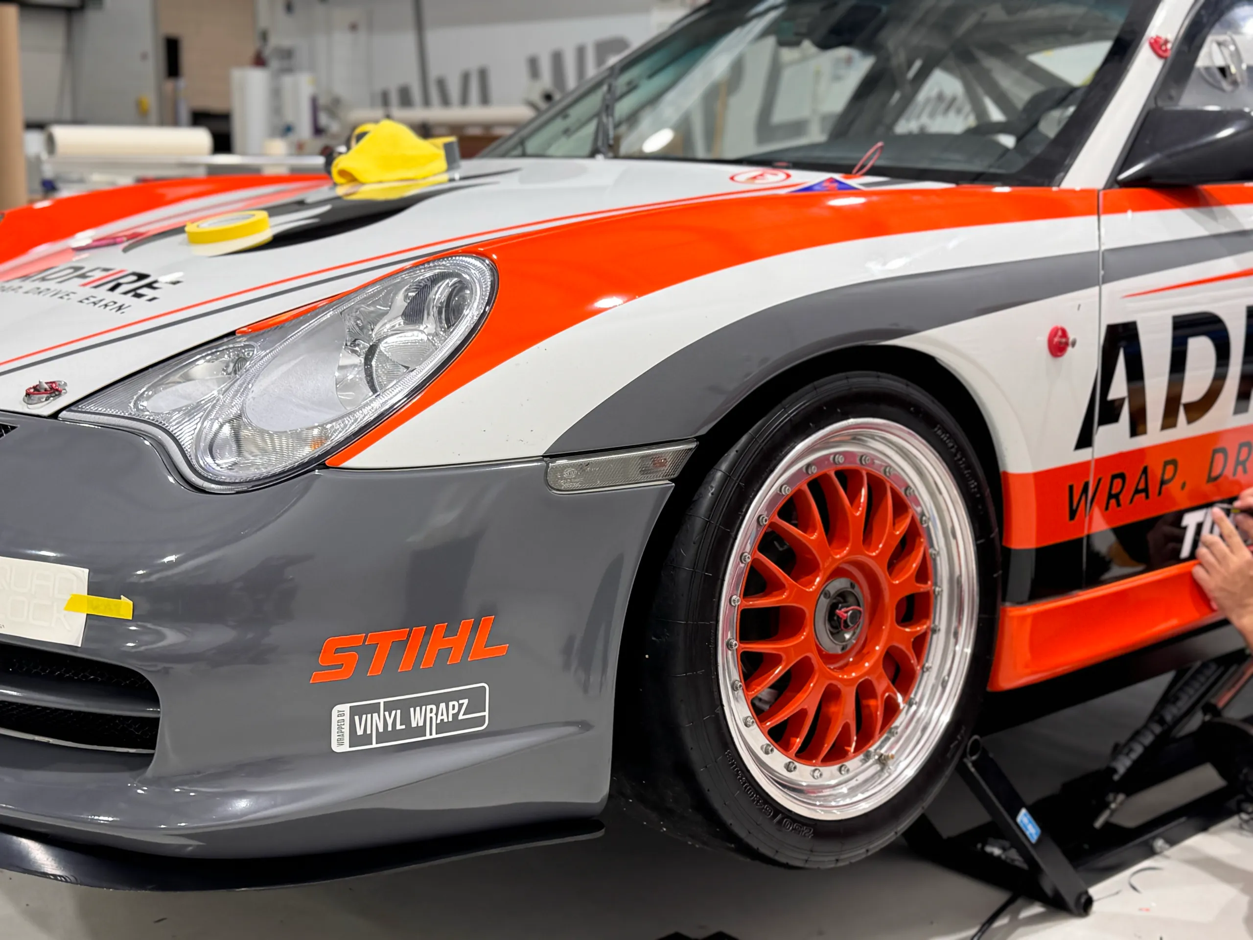 Porsche front wheel and guard with Adfire graphics while an installer applies side lettering