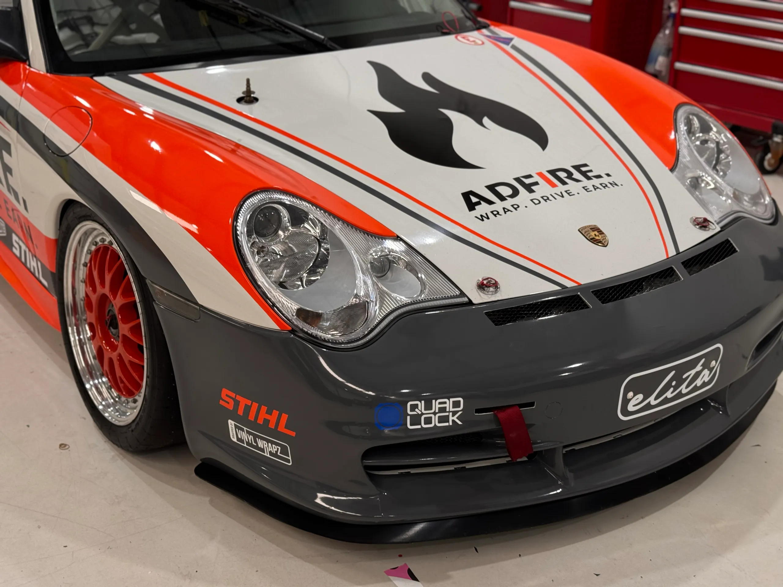 Adfire flame logo on the Porsche bonnet above a grey front bumper and orange wheels