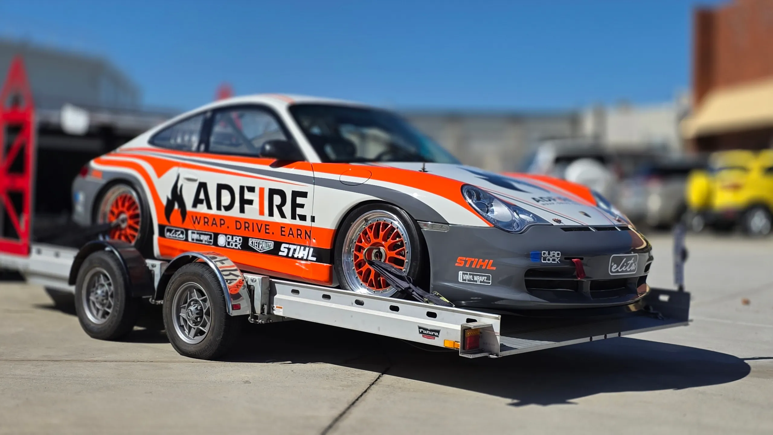 Orange, white and grey Adfire Porsche GT3 on a car trailer outside the workshop