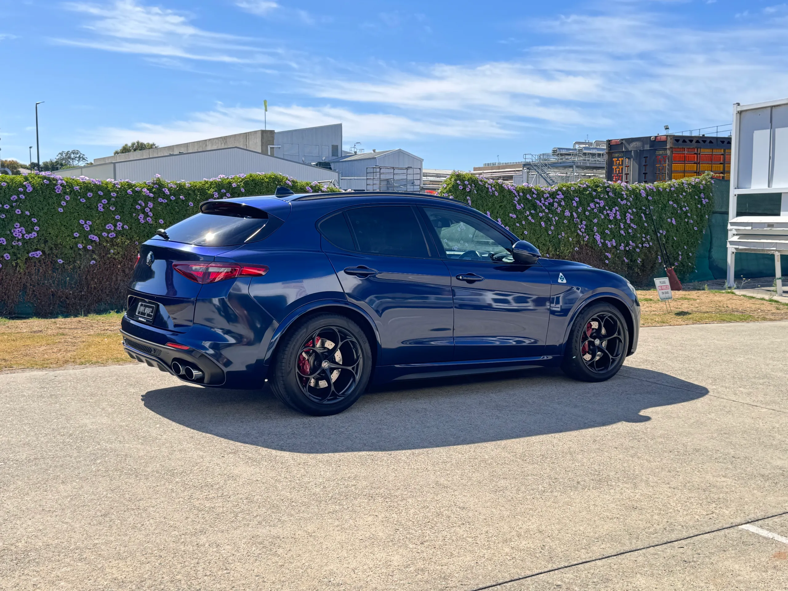 Blue-black Alfa Romeo Stelvio viewed from the rear quarter outdoors, showing its side and black wheels