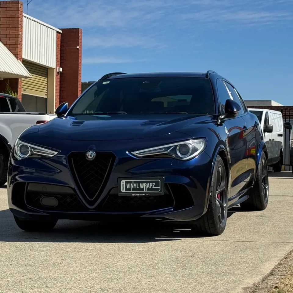 Low front-quarter view of a blue-black Alfa Romeo Stelvio outside the workshop