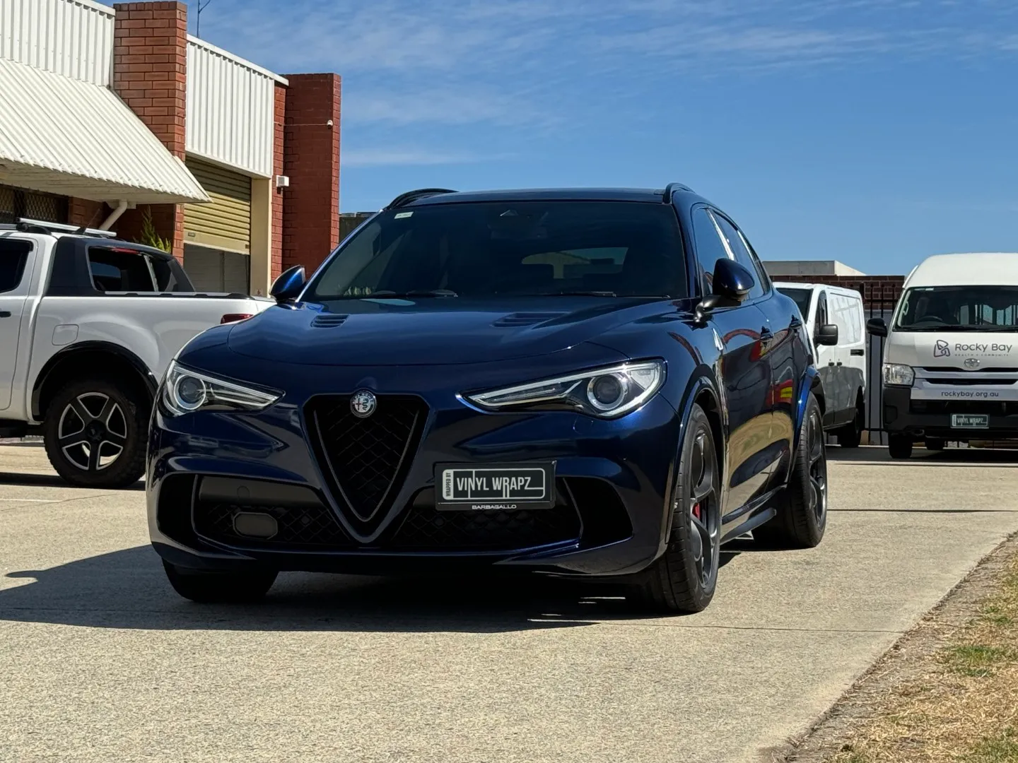 Low front-quarter view of a blue-black Alfa Romeo Stelvio outside the workshop