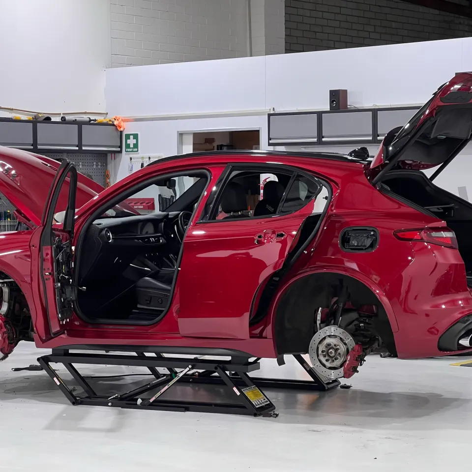 Red Alfa Romeo Stelvio on a lift with wheels and trim removed and doors open during preparation