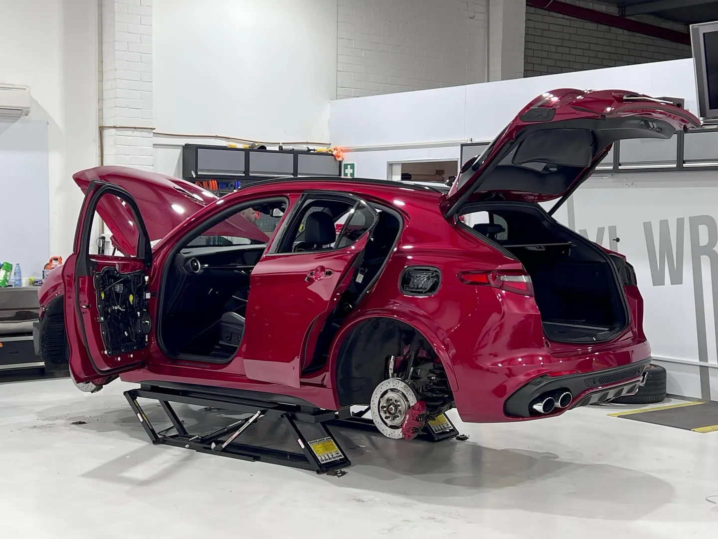 Rear quarter of a red Alfa Romeo Stelvio on a lift, with doors, bonnet and tailgate open during preparation