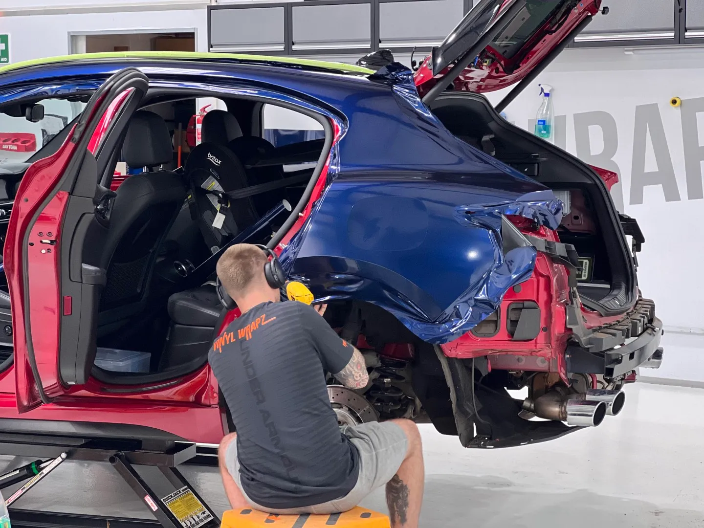 Back-facing installer fitting blue film to an Alfa Romeo Stelvio rear quarter, with original red paint exposed