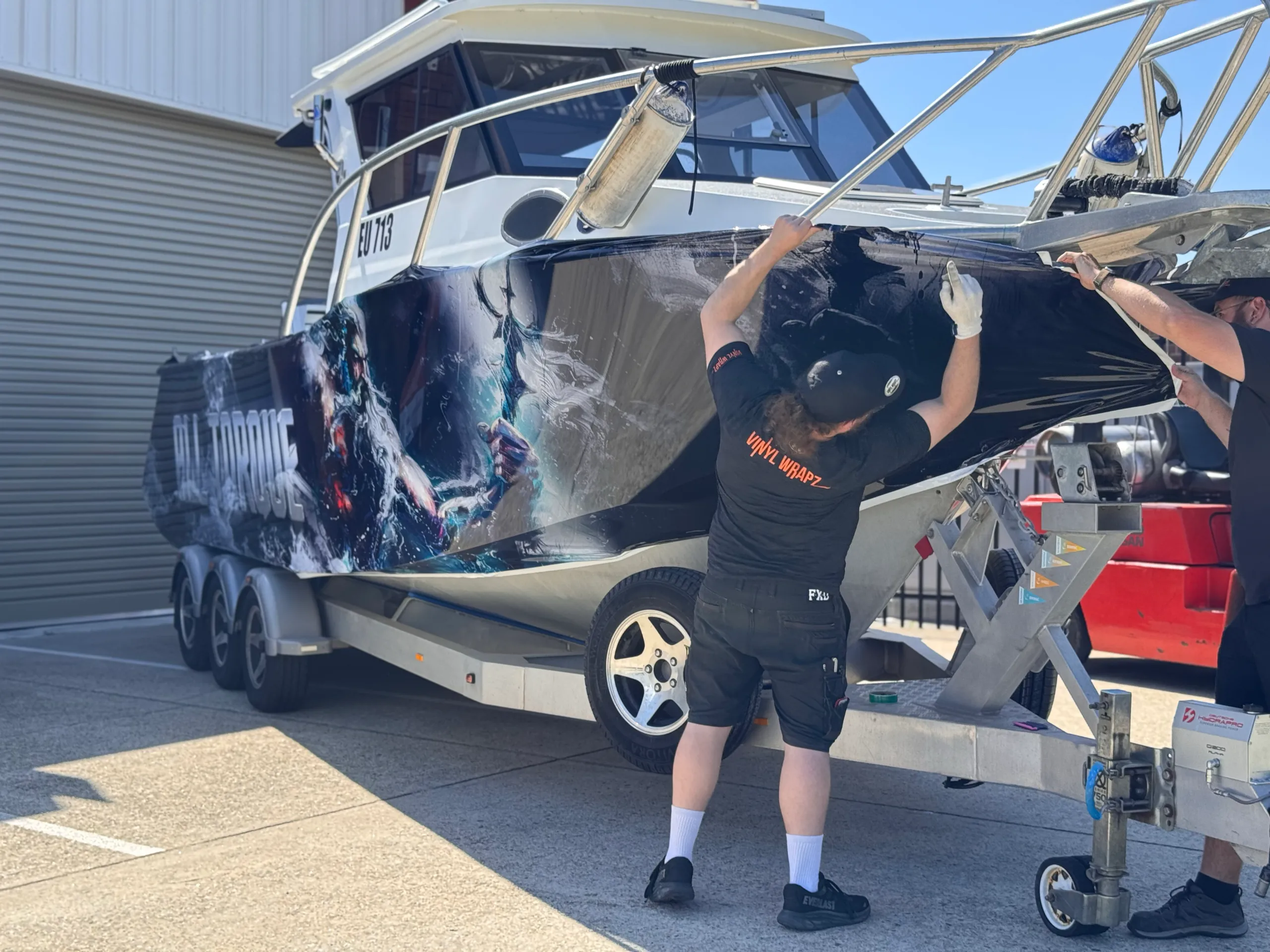 Installers stretching Poseidon artwork around the Razerline Olympian bow