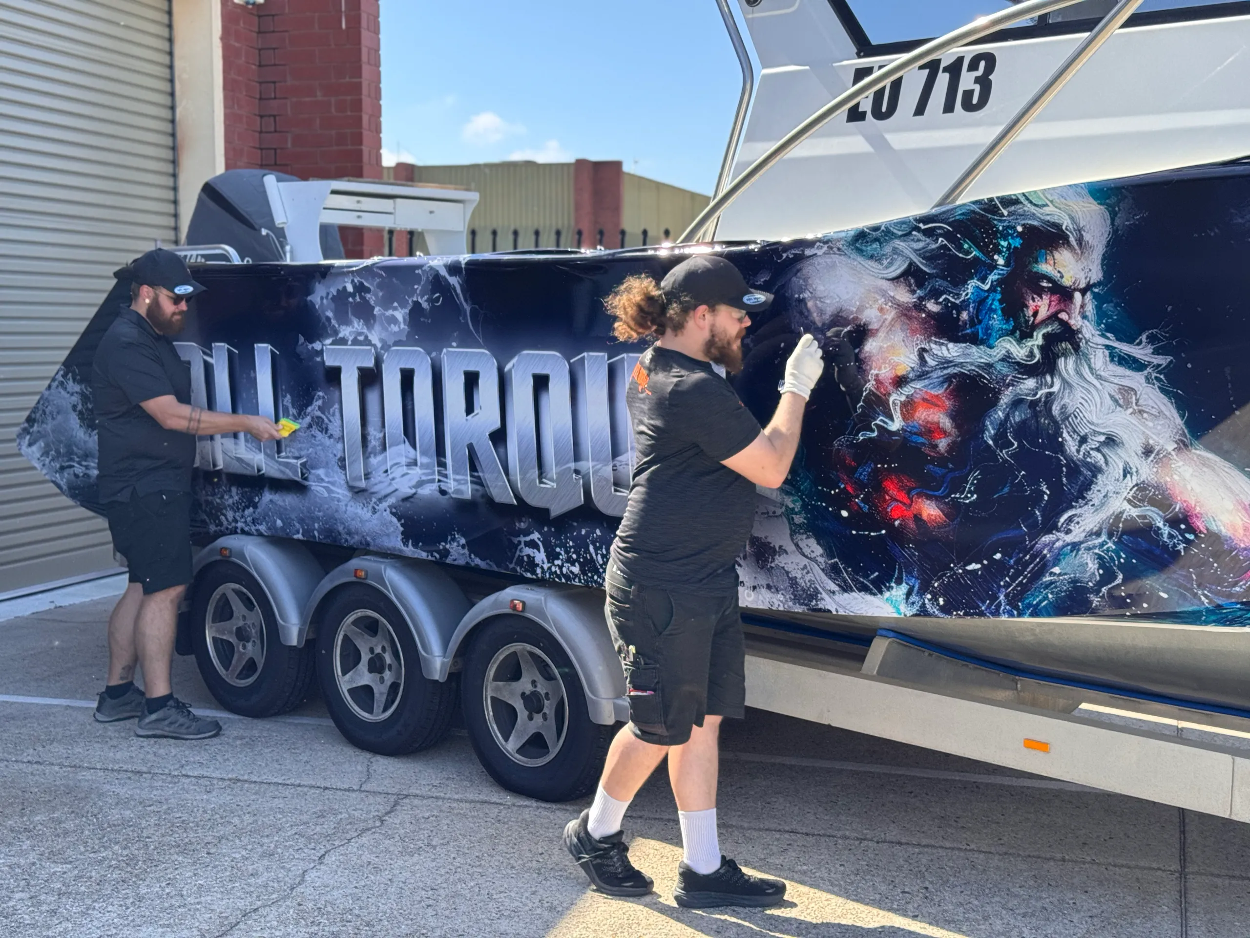 Installers smoothing the All Torque and Poseidon graphics along the boat hull