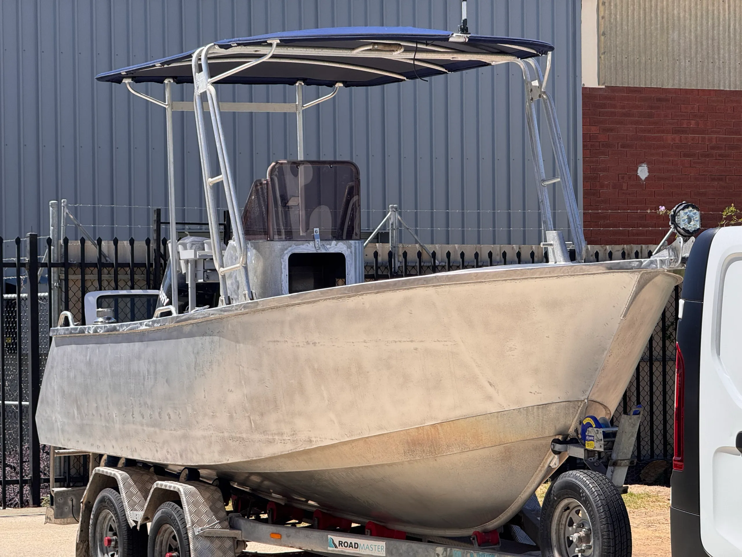 Bare aluminium centre-console boat on its trailer outside before the wrap was fitted