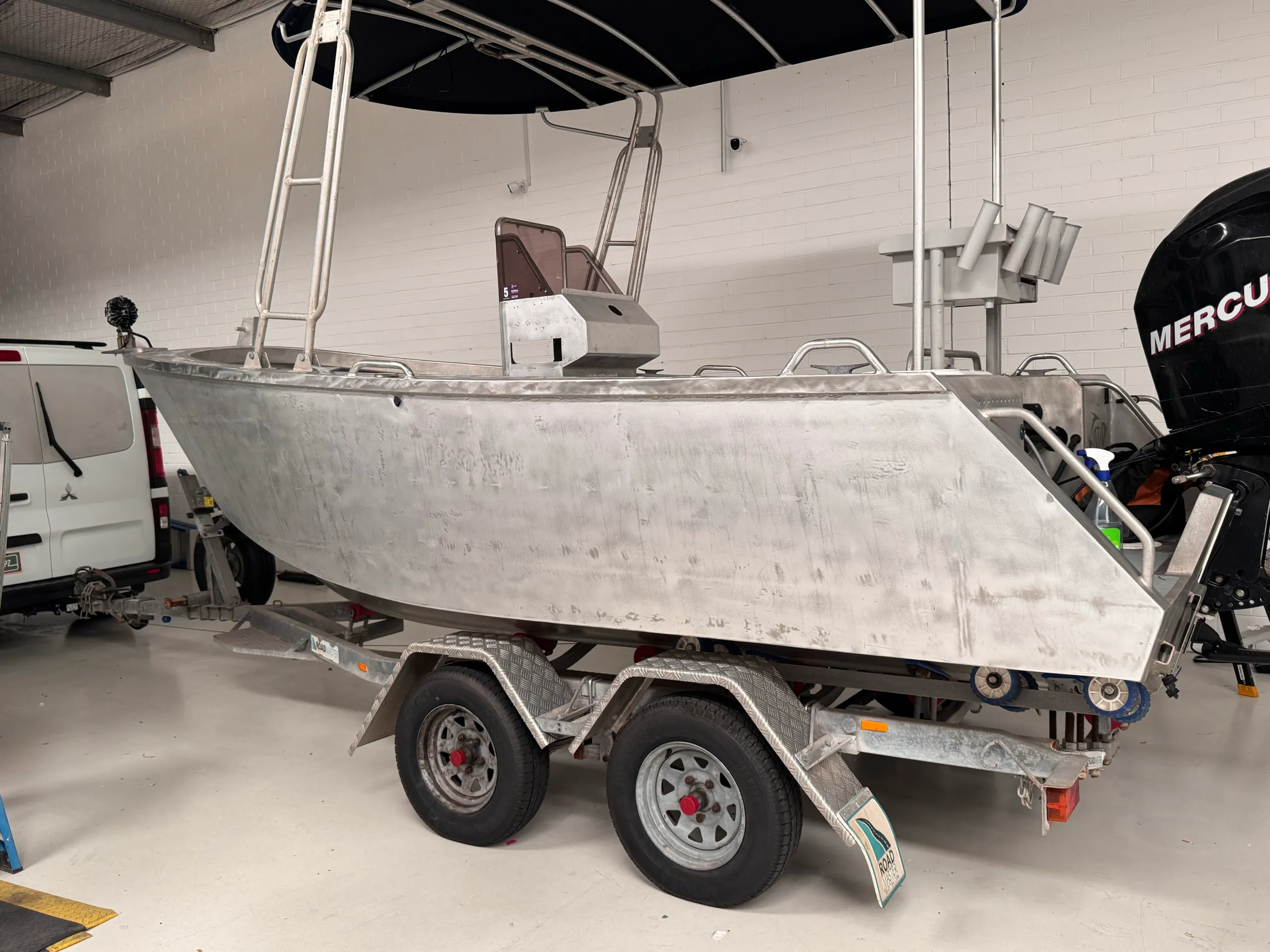 Unwrapped aluminium boat hull and Mercury outboard inside the workshop