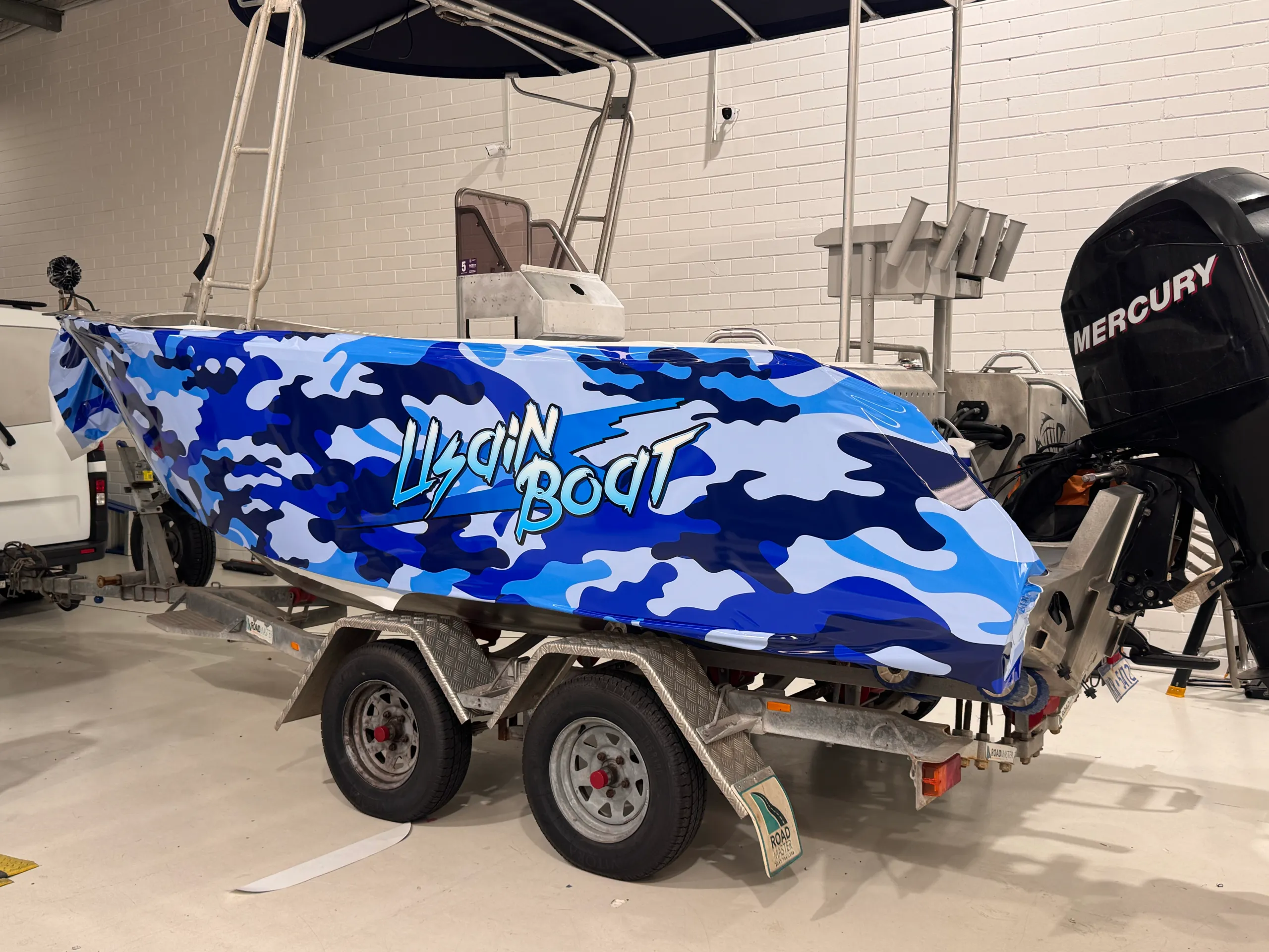 Blue camouflage wrap film positioned along the aluminium boat hull before trimming