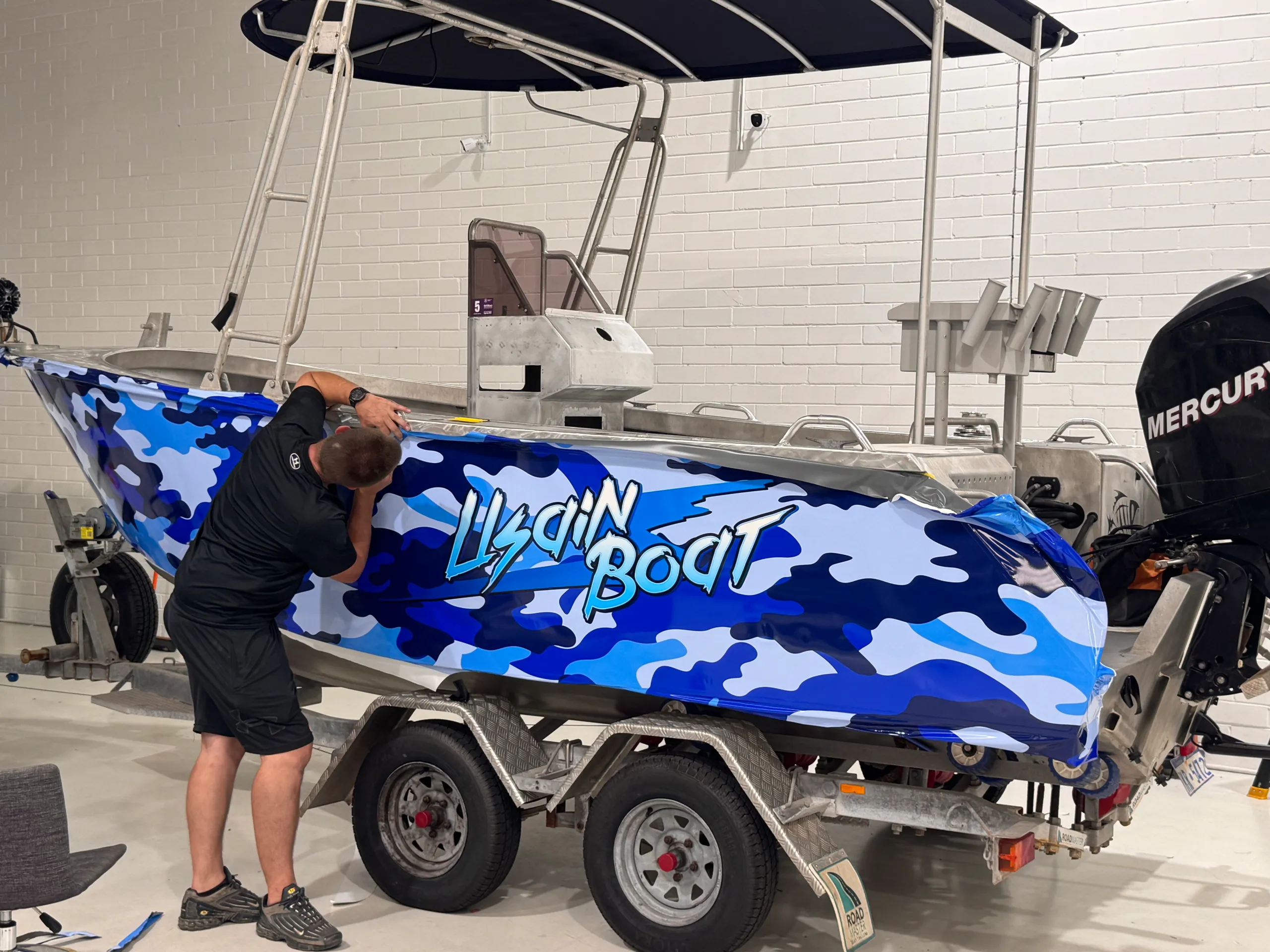 Installer fitting blue camouflage graphics along the aluminium boat hull