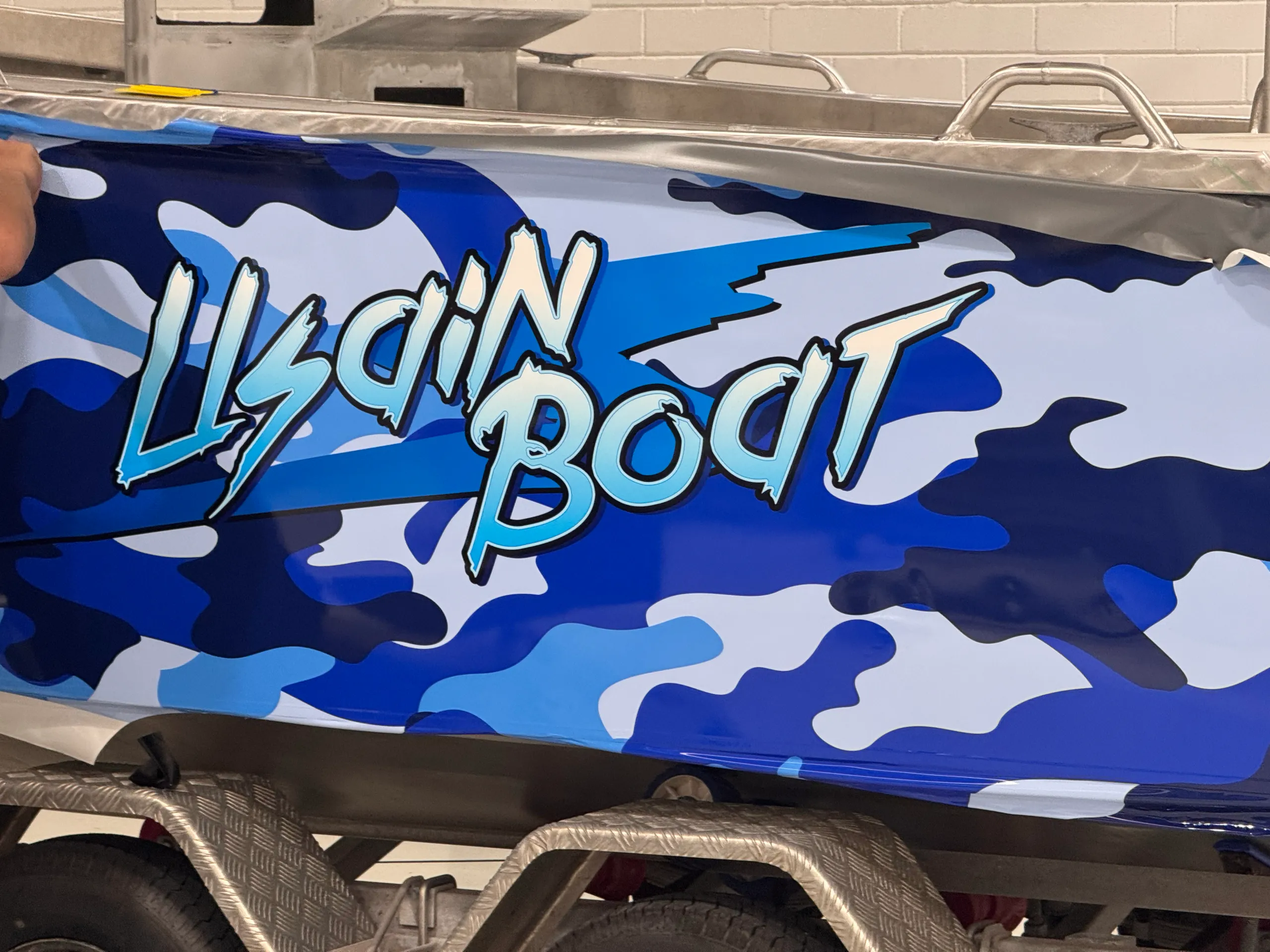 Close view of lettering across blue camouflage film during boat-wrap installation