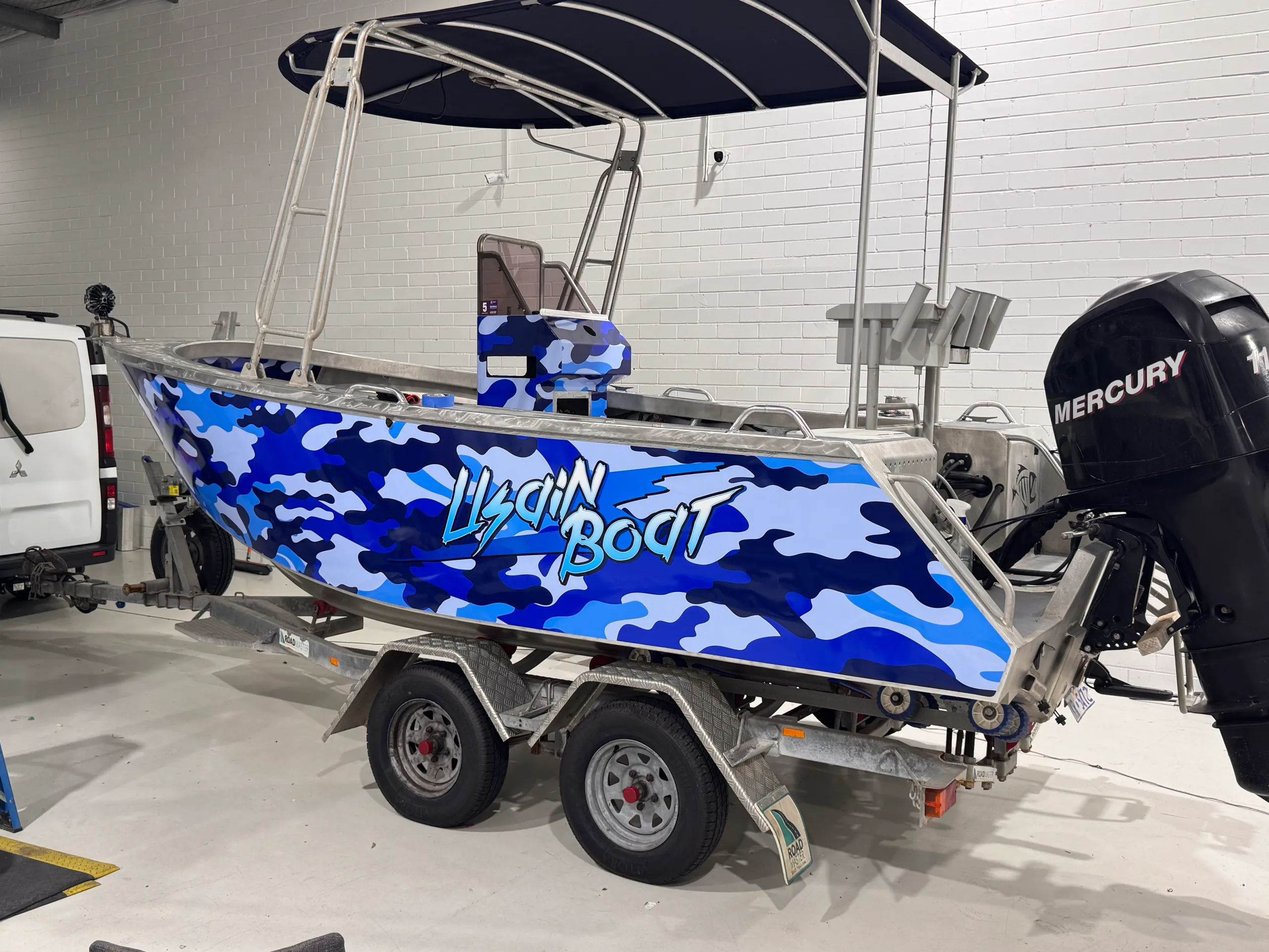 Aluminium centre-console boat with blue camouflage graphics and a Mercury outboard in the workshop
