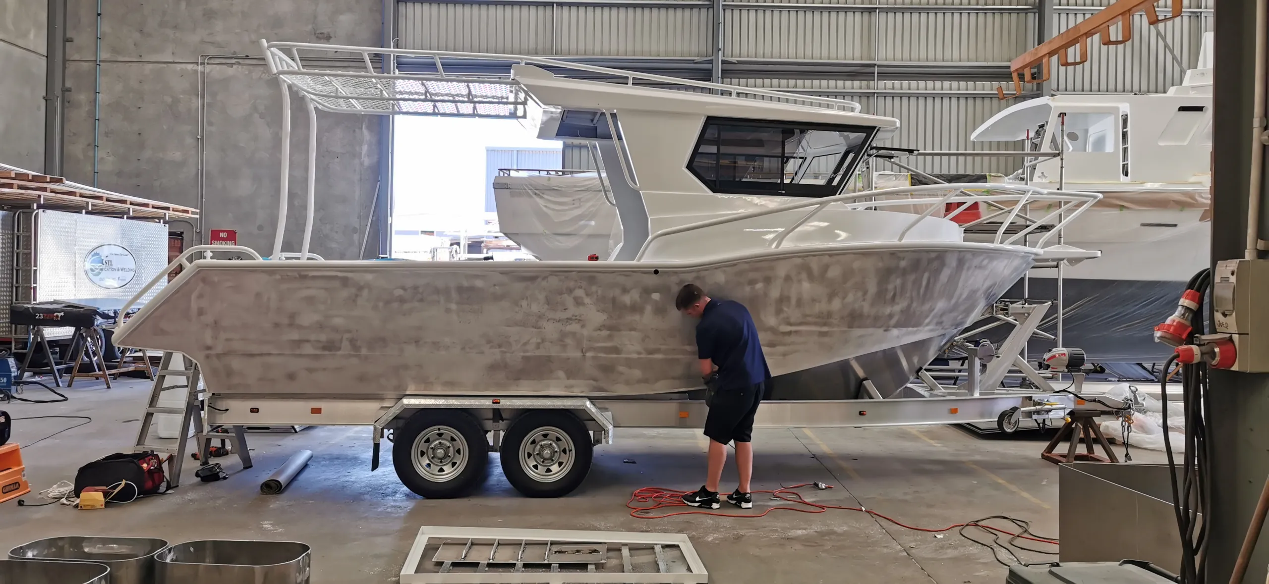 Installer preparing the bare aluminium hull of a cabin boat on its trailer