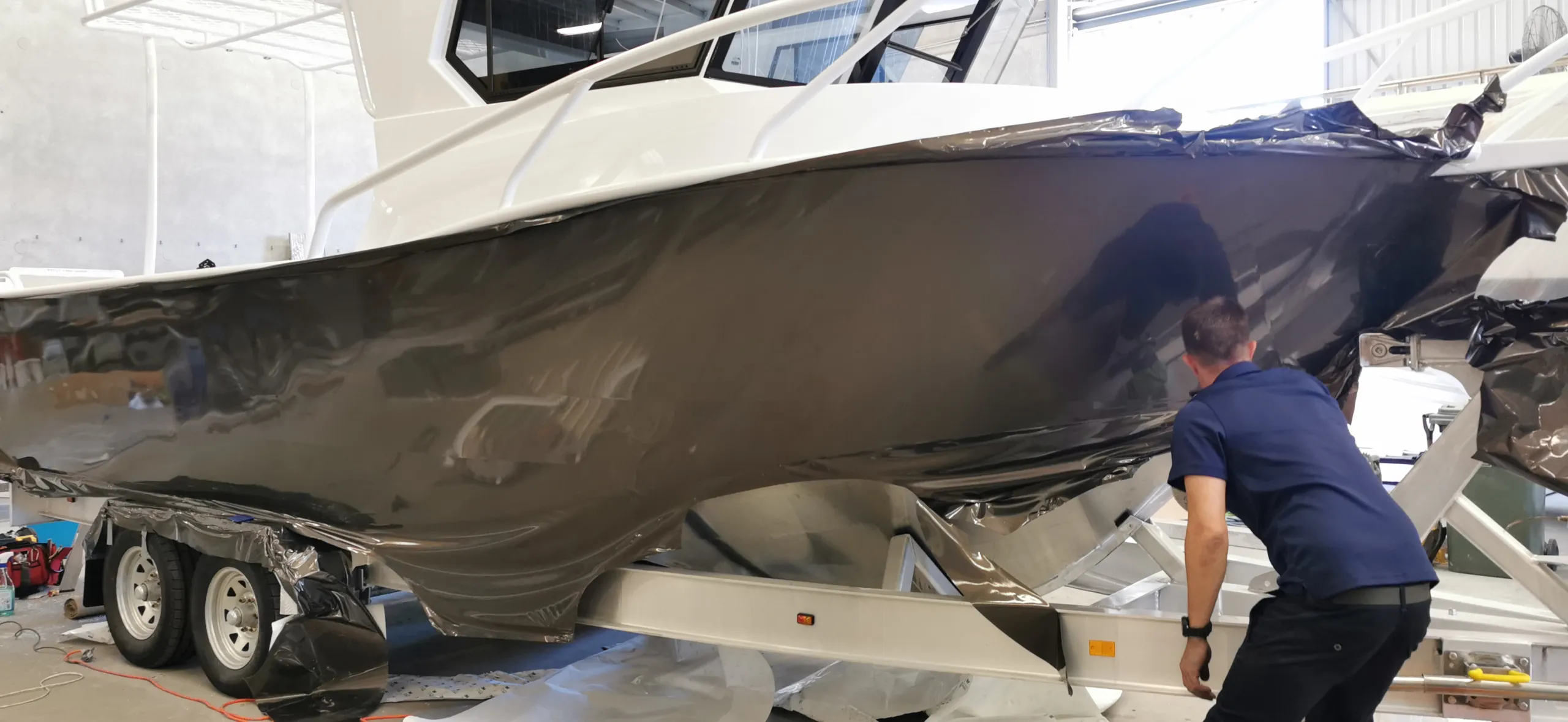 Installer facing the hull while fitting dark charcoal film around the boat bow