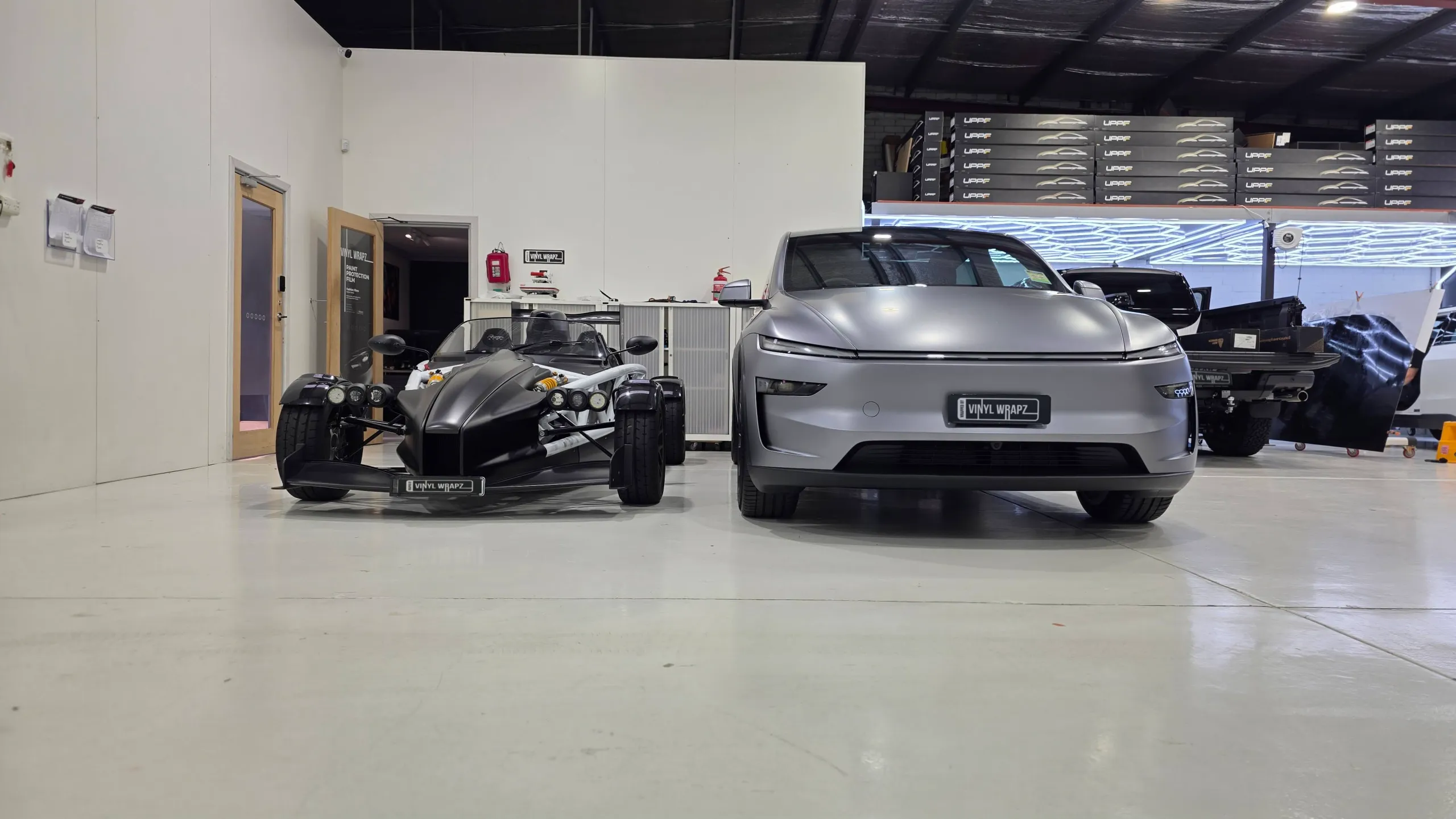 Ariel Atom and grey Tesla parked side by side in the workshop
