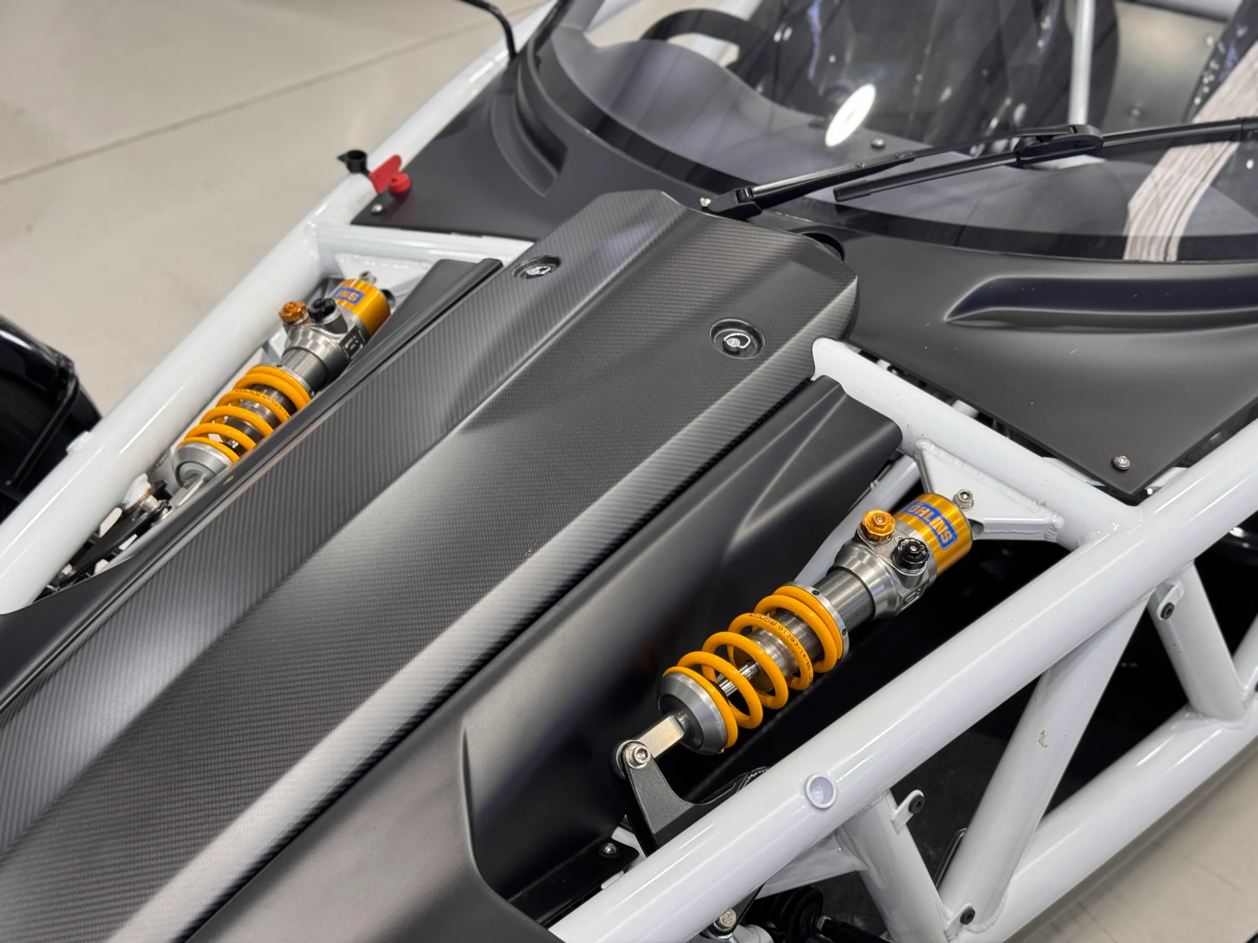 Carbon-patterned Ariel Atom nose panel between exposed yellow front suspension springs