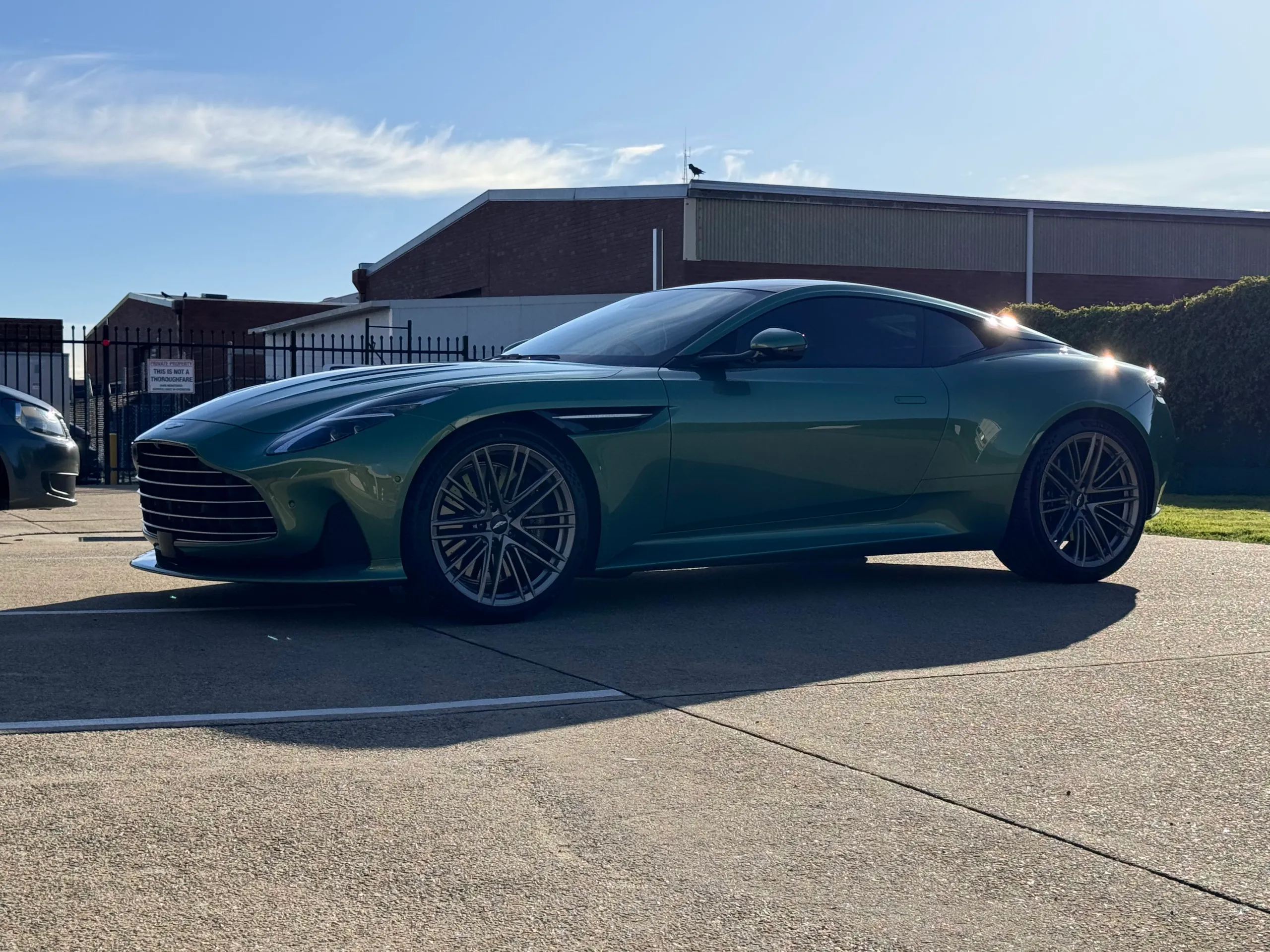 Side view of the green Aston Martin DB12 with strong sunlight across its roof and rear quarter