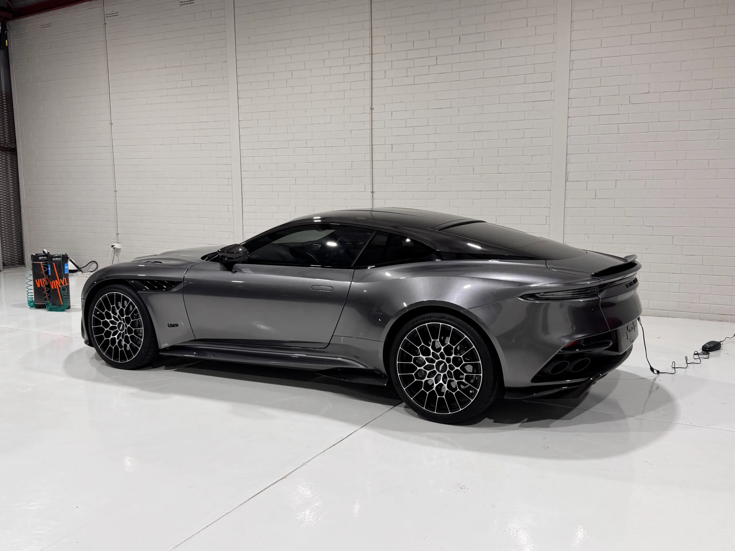 Grey Aston Martin DBS rear quarter and side profile with a cable connected in the workshop