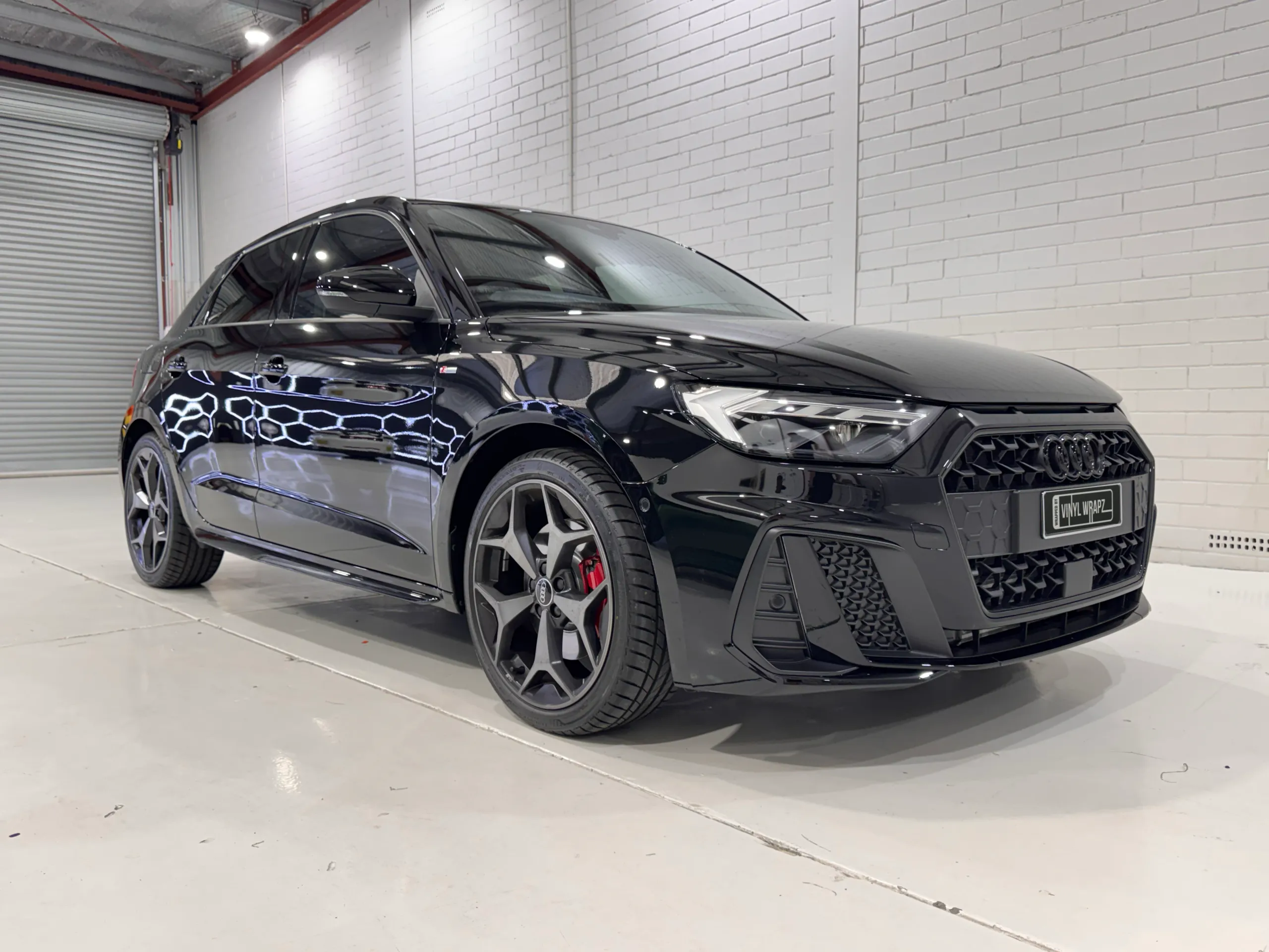 Gloss black Audi A1 with grey alloy wheels and red brake calipers in the workshop