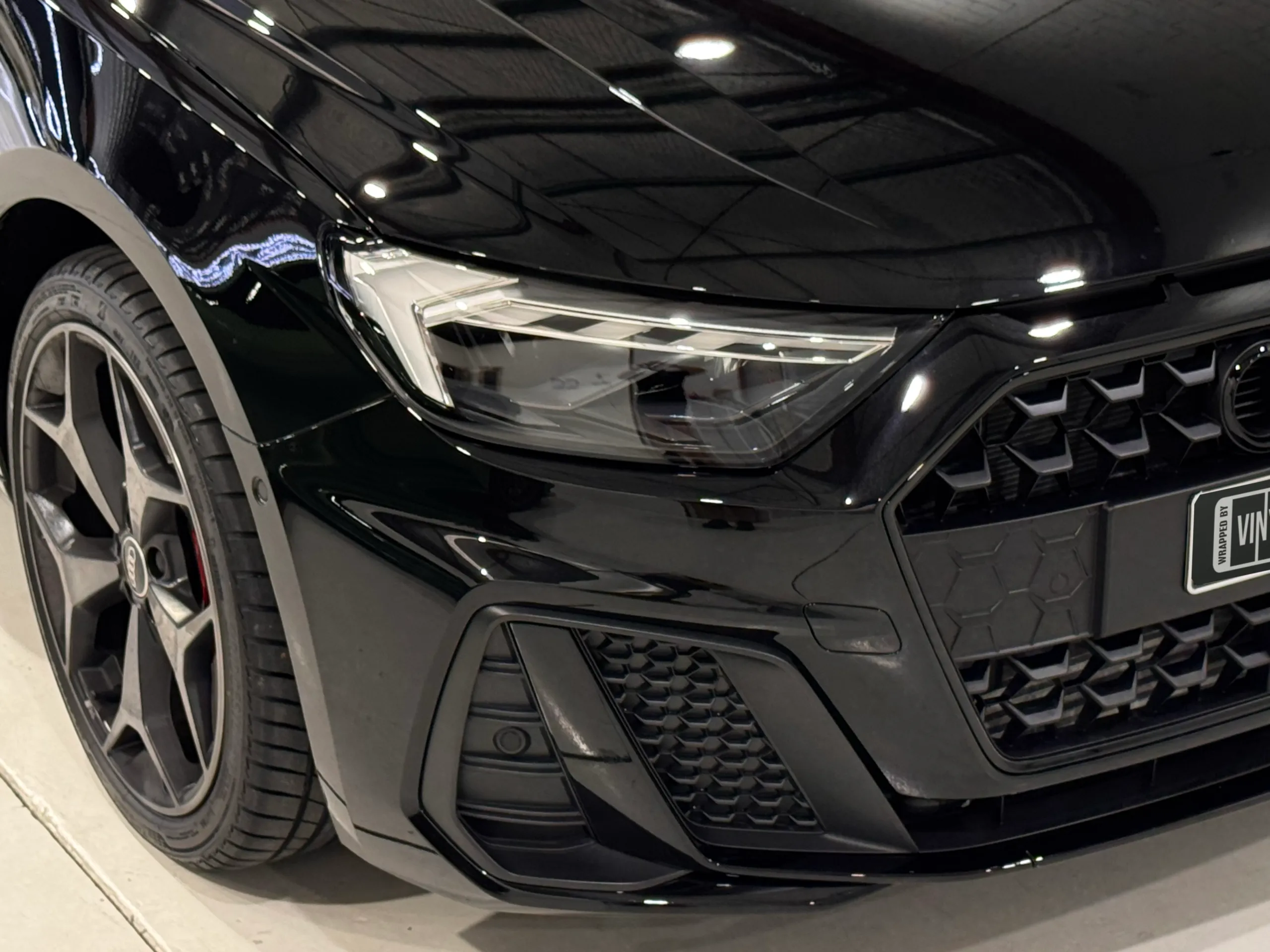 Audi A1 headlight, grille and gloss black bonnet reflecting workshop lights