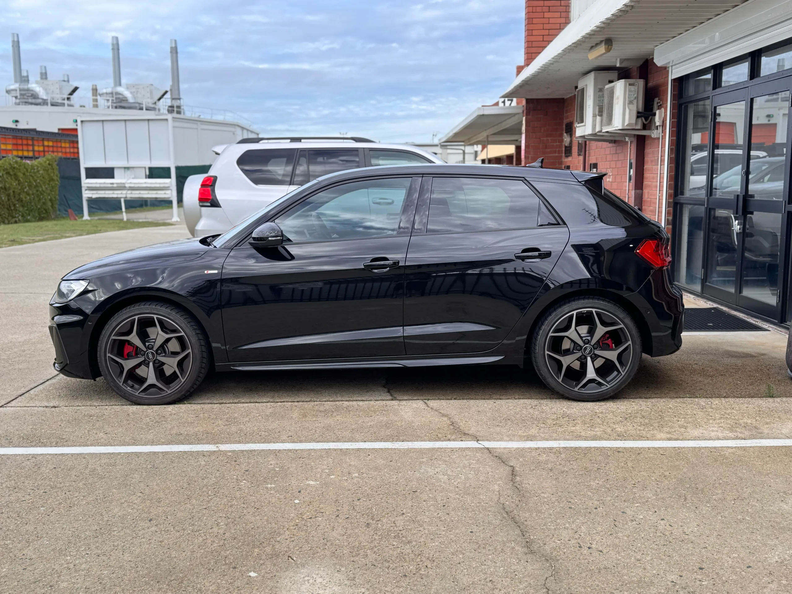 Full side profile of a gloss black Audi A1 outside the workshop