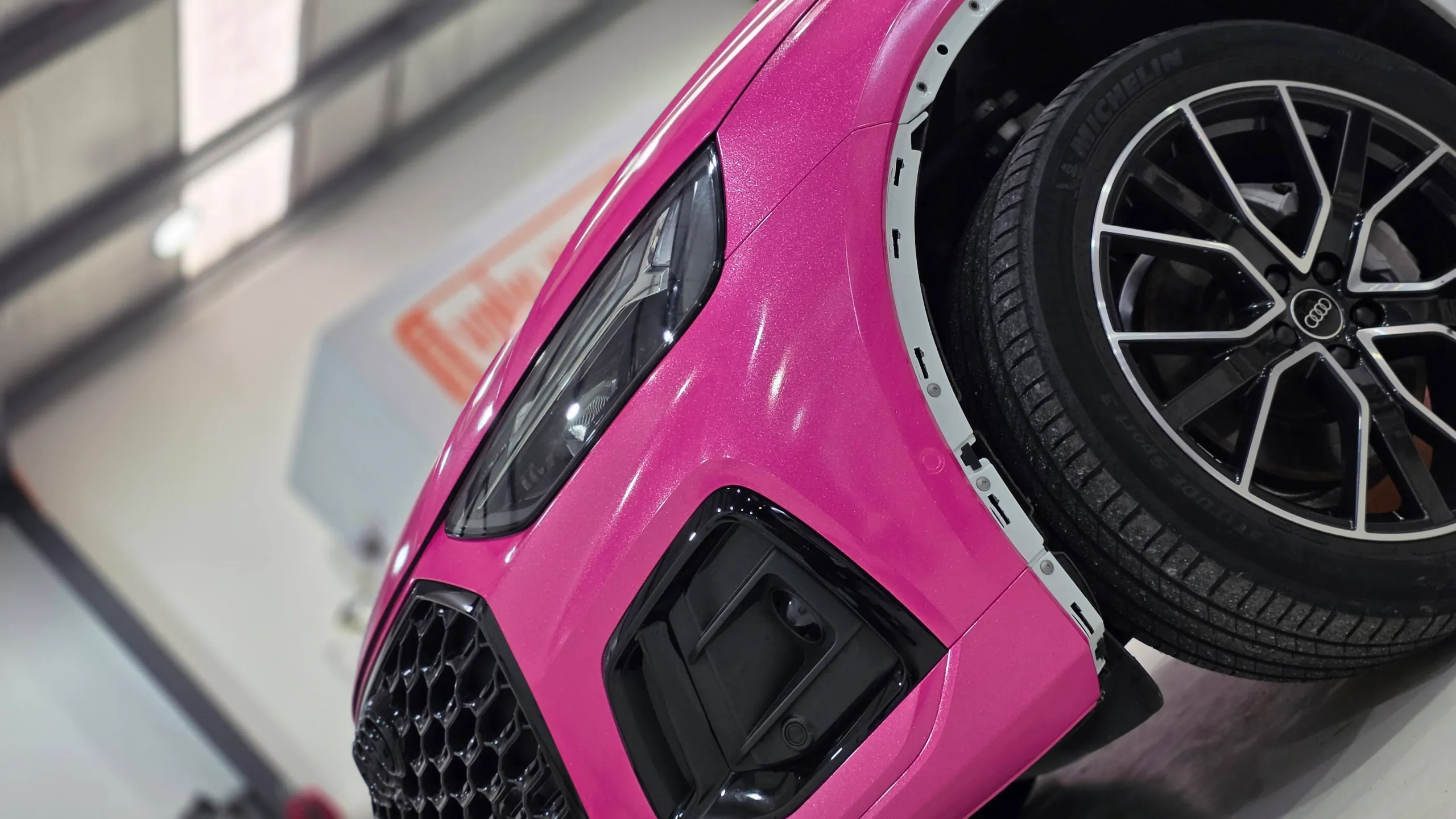 Tilted view of a sparkling pink Audi Q5 Sportback front corner with wheel-arch trim removed during wrapping