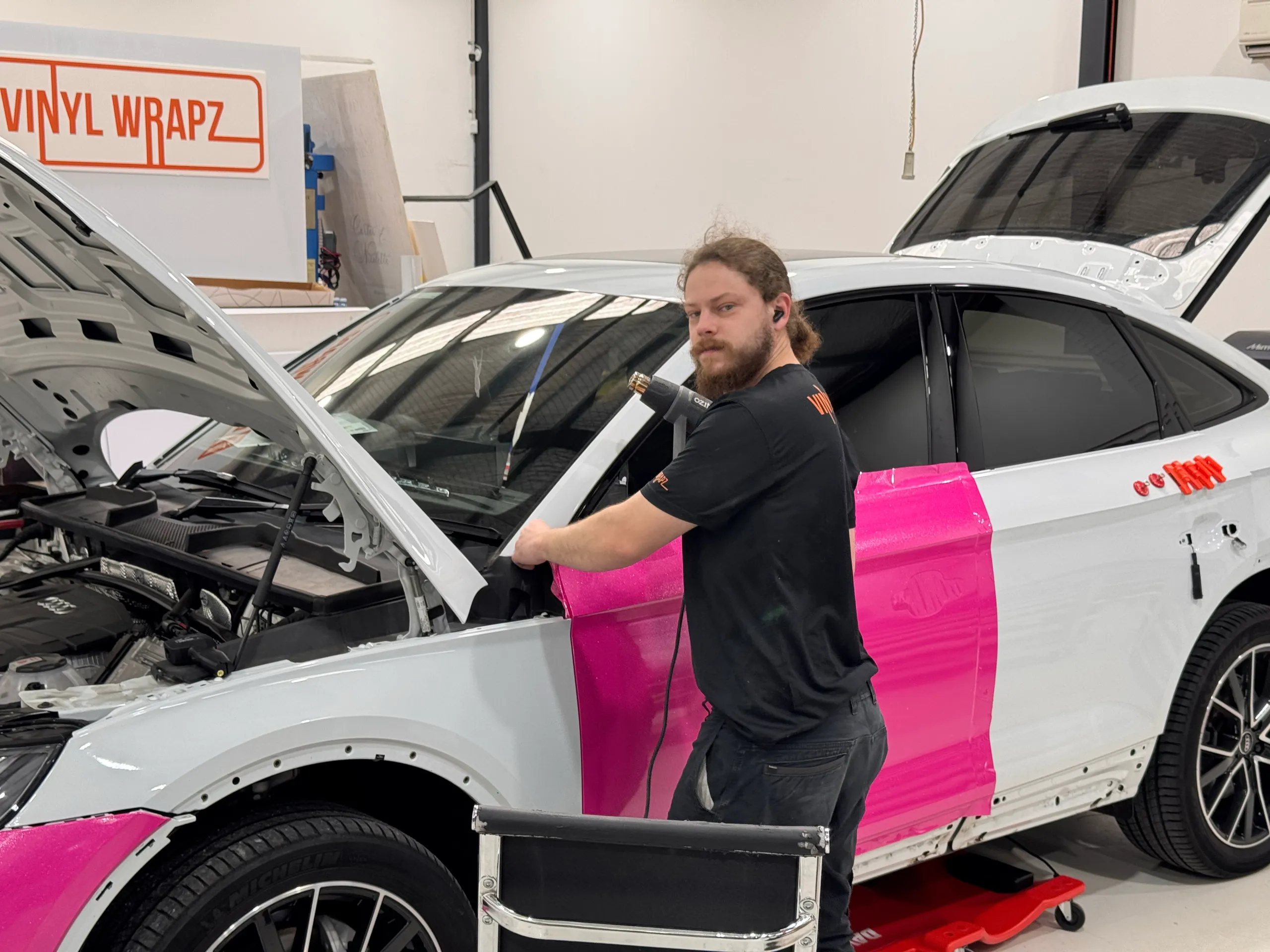 Installer beside a white Audi Q5 Sportback with pink film on the door during wrapping