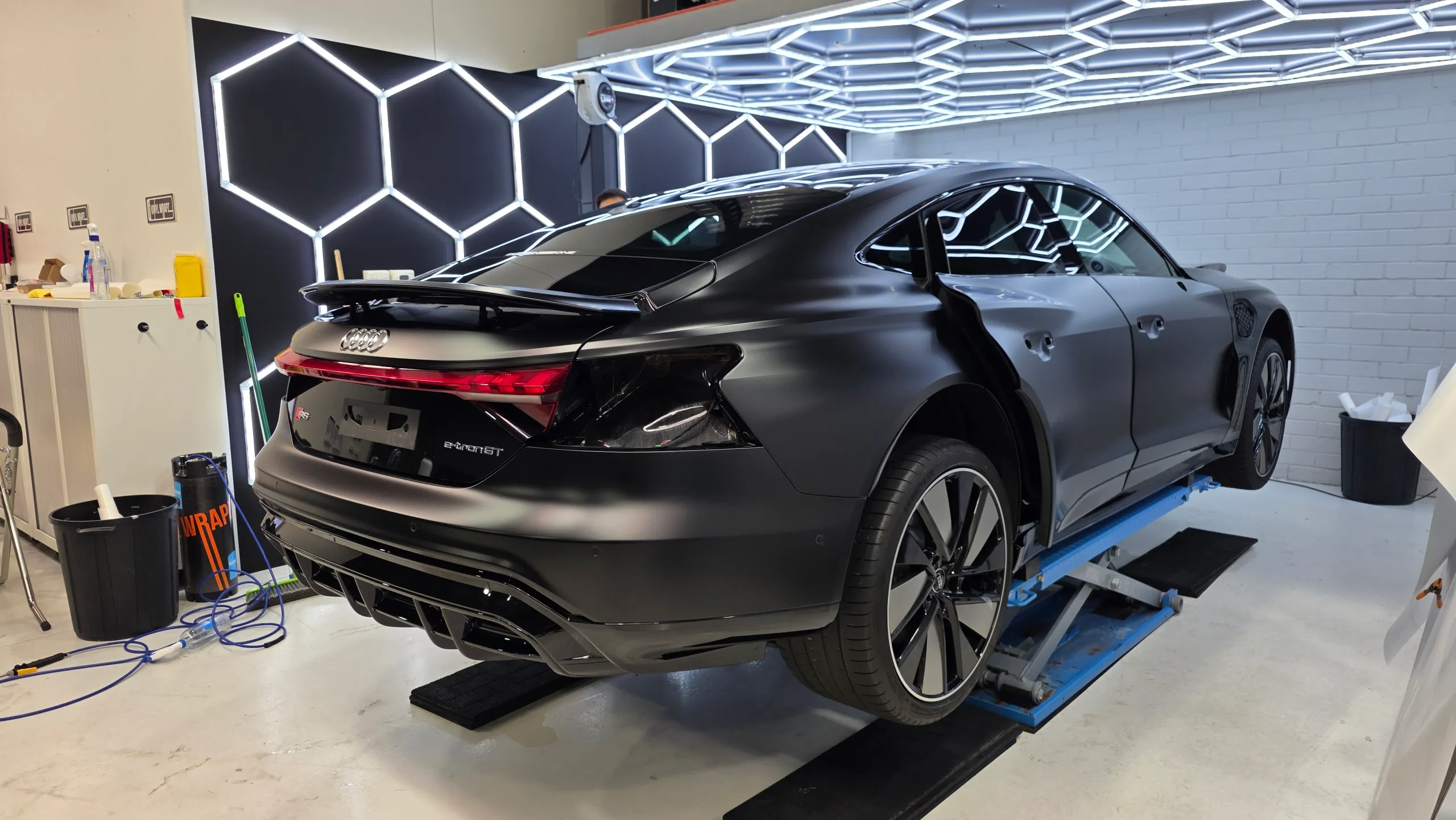 Audi RS e-tron GT on a workshop lift during film installation, with a person beyond the roof