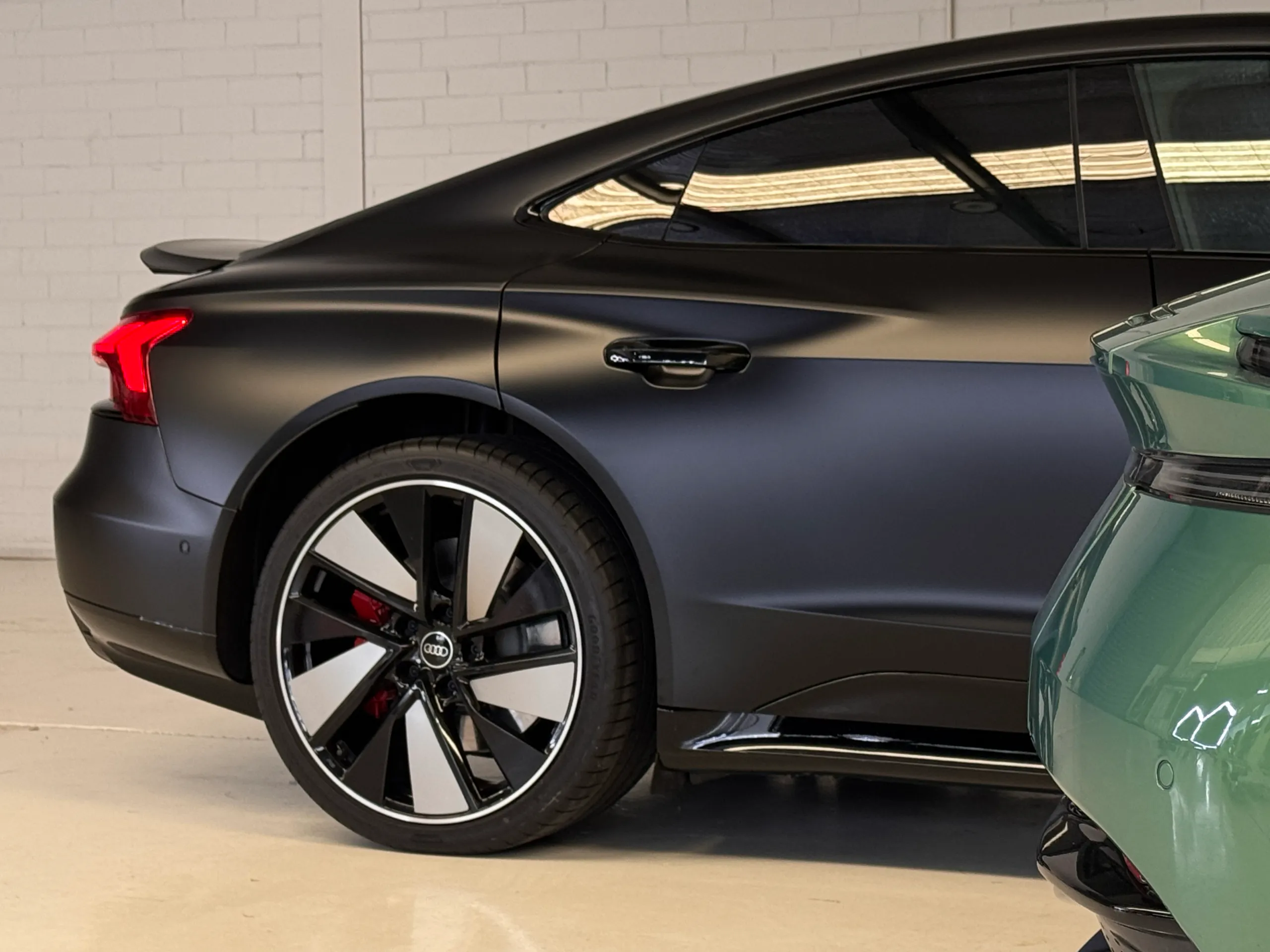 Matte black Audi RS e-tron GT rear wheel and door, partly obscured by another car