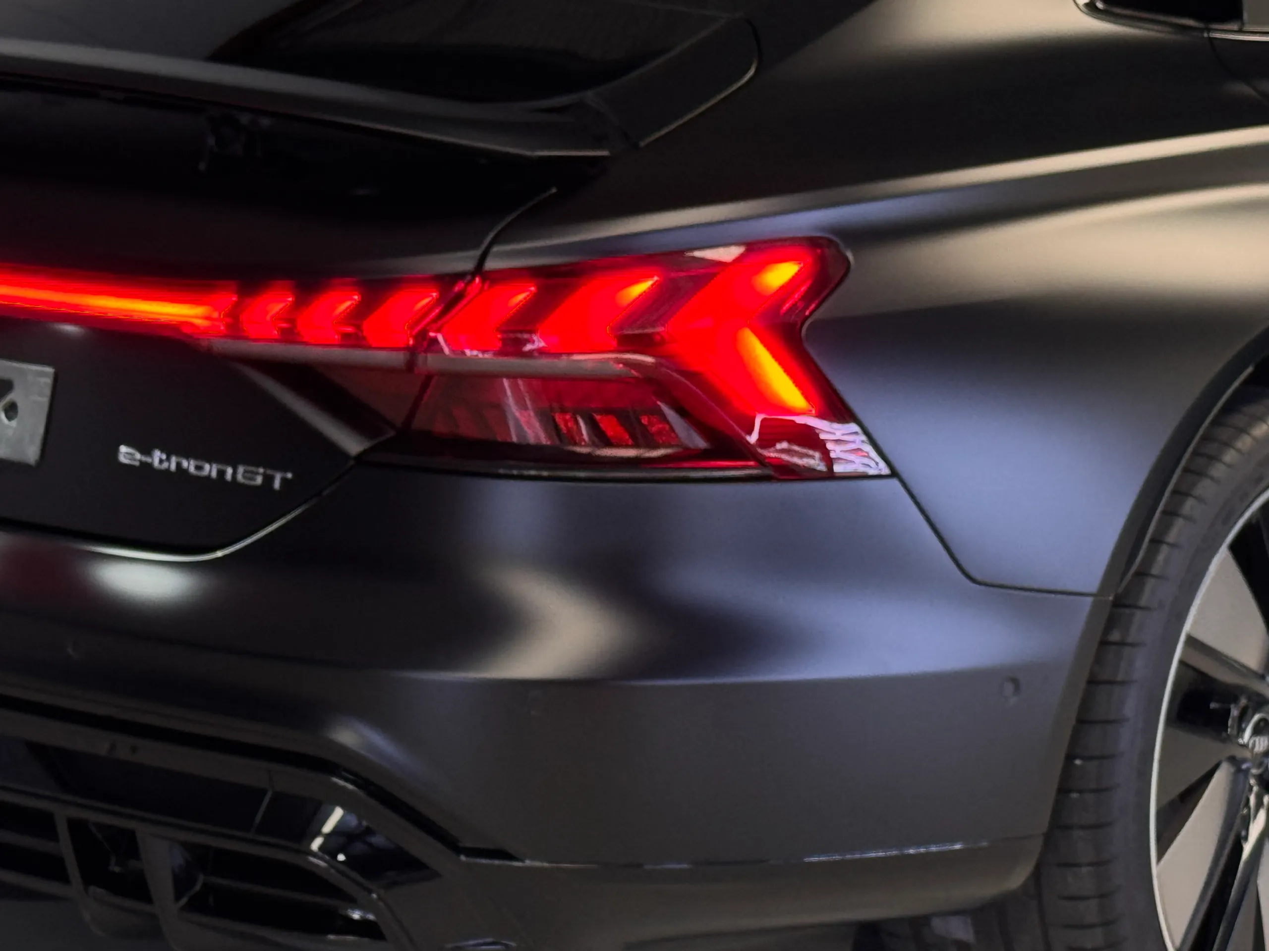Audi e-tron GT badge beside the illuminated rear light bar on matte black bodywork