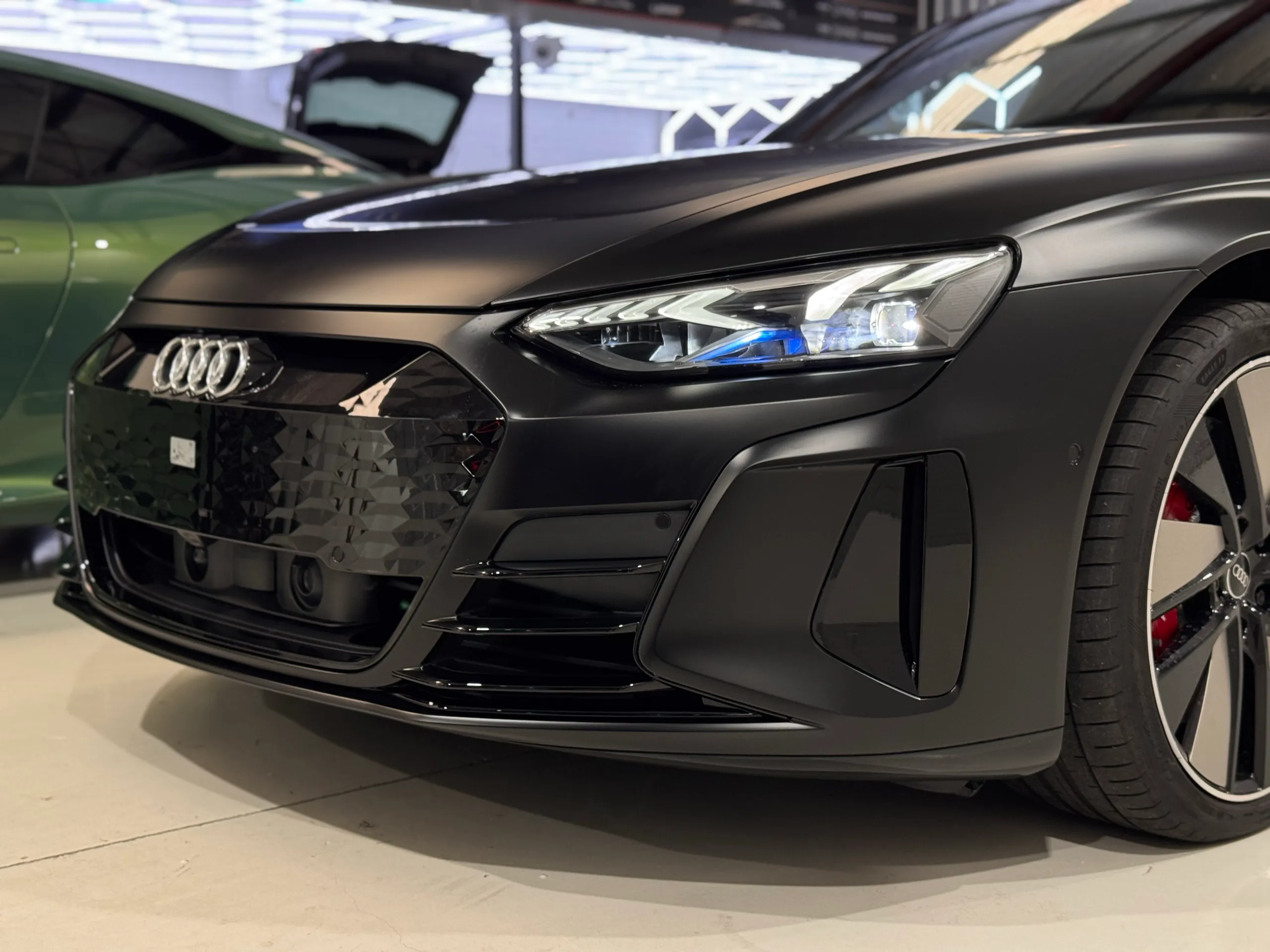 Low front-quarter detail of the matte black Audi RS e-tron GT with its headlight illuminated