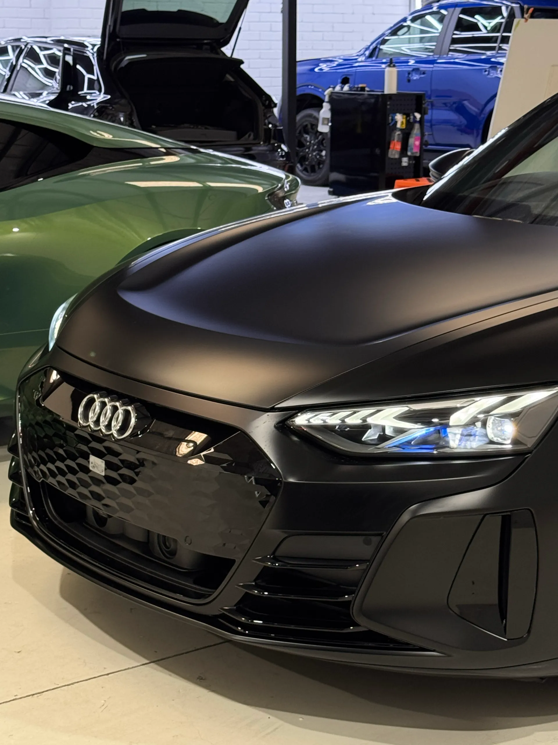 Matte black Audi RS e-tron GT front corner beside a green car in the workshop