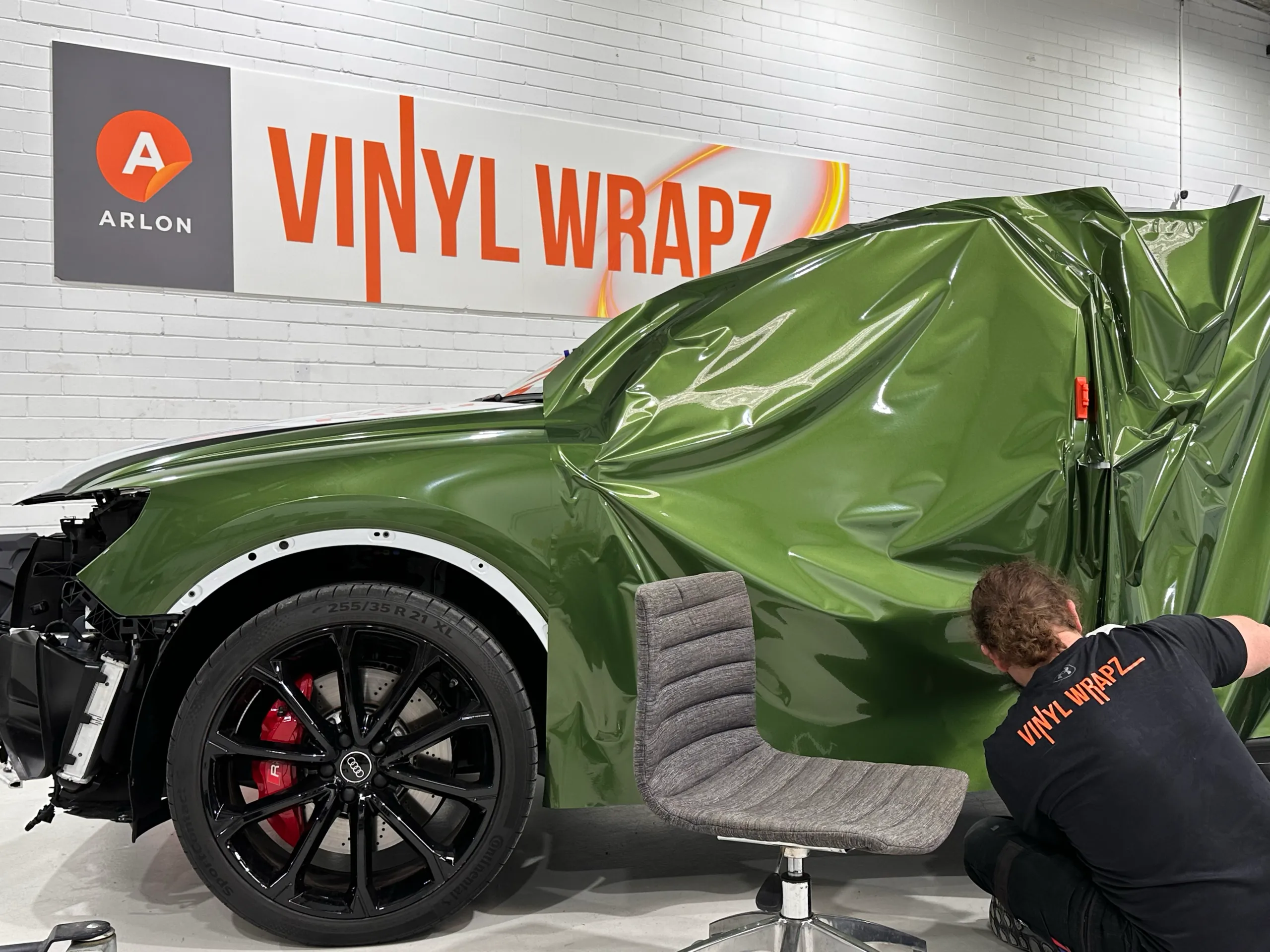 Back-facing installer positioning green wrap film over an Audi RS Q3 Sportback side with the doors removed
