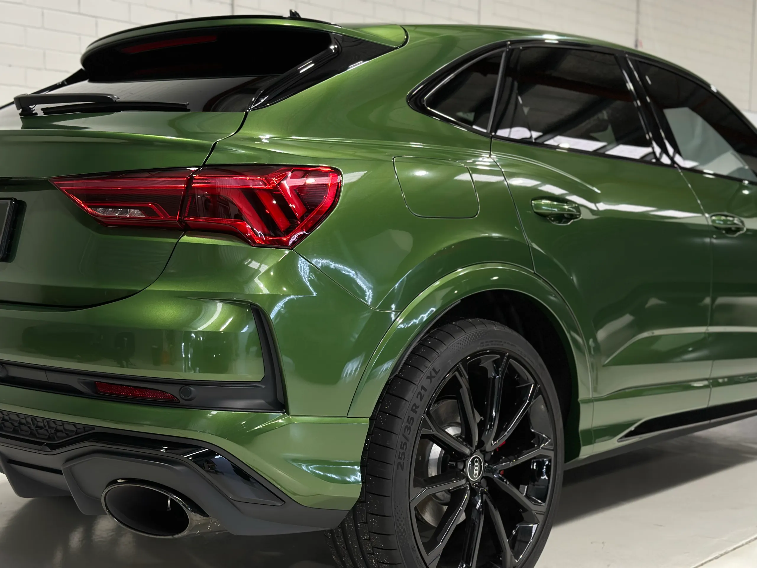 Metallic green Audi RS Q3 Sportback rear quarter, black wheel and red tail light in the workshop