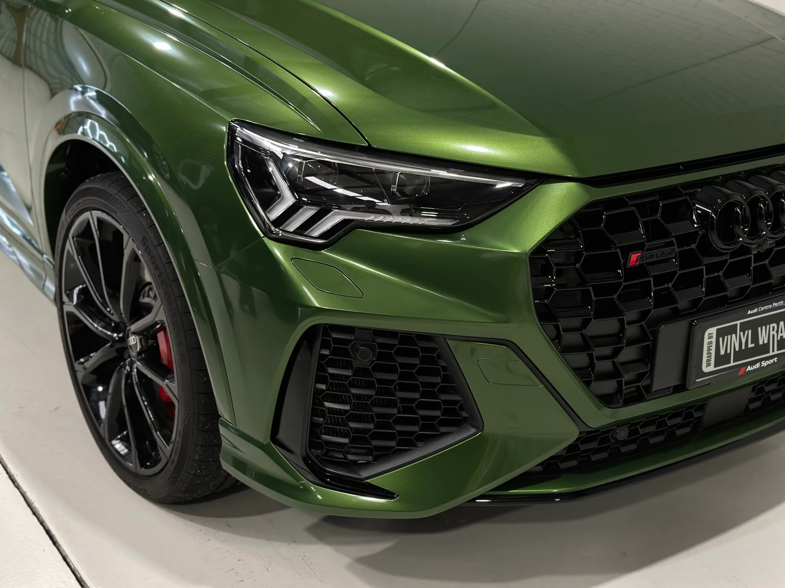 Elevated front detail of a green Audi RS Q3 Sportback, showing its headlight and black grille
