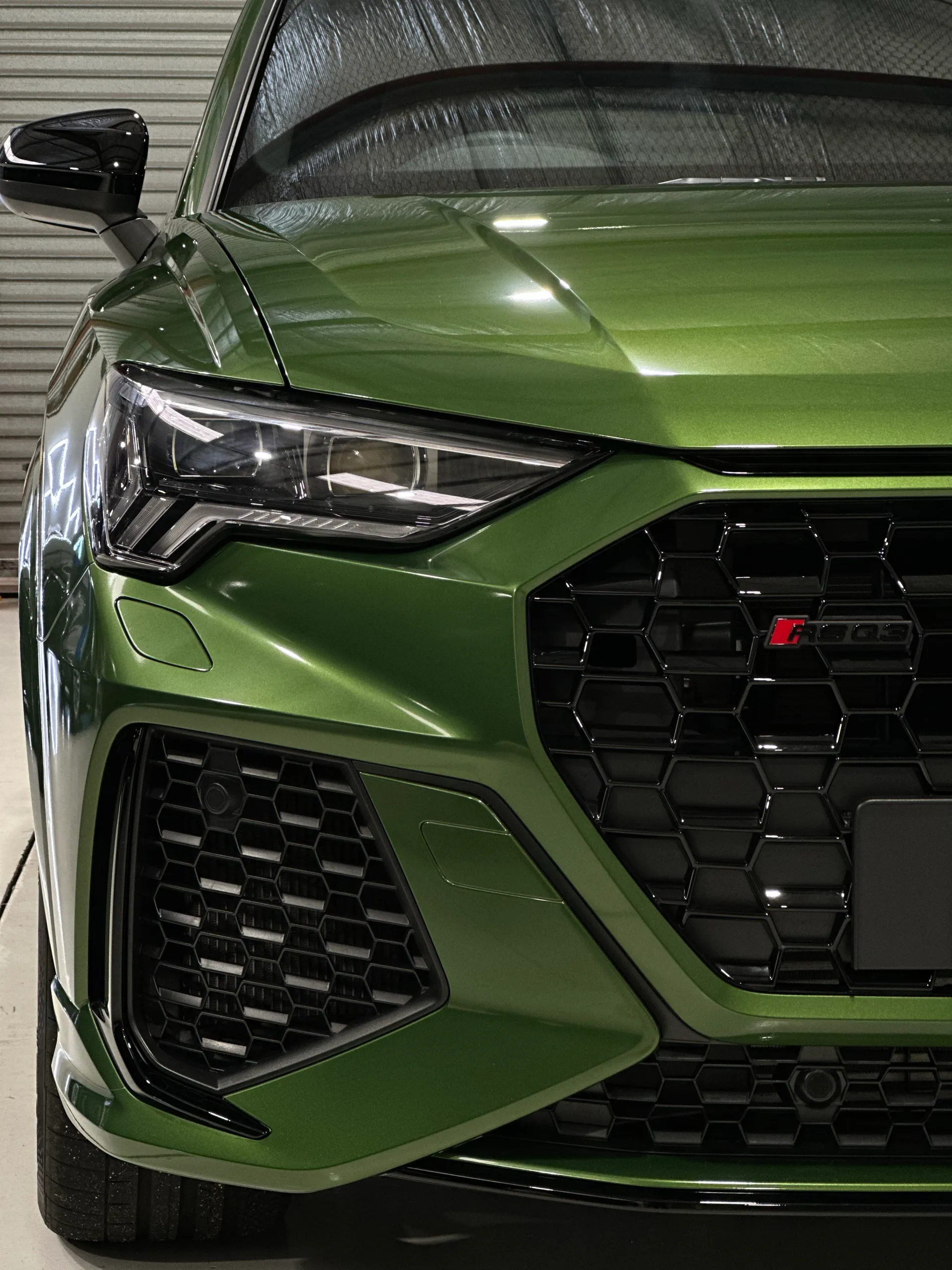 Front detail of a metallic green Audi RS Q3 Sportback bonnet, headlight and grille badge