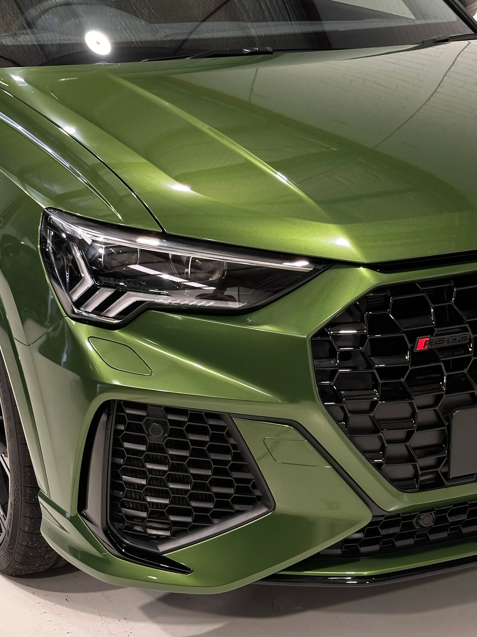 Green Audi RS Q3 Sportback bonnet and headlight beneath reflected workshop lights