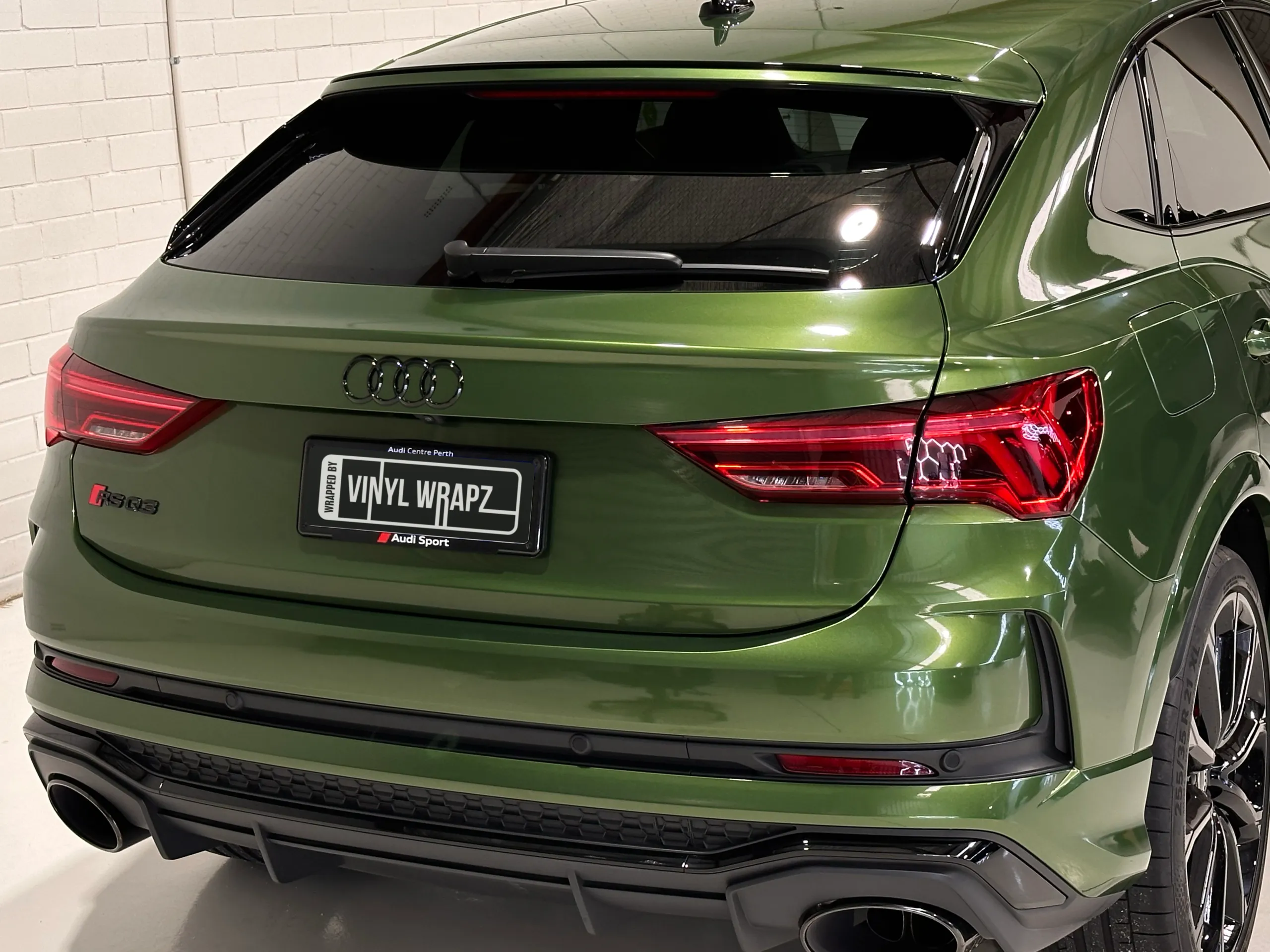 Rear of a metallic green Audi RS Q3 Sportback, showing the tailgate, red lights and twin exhaust outlets