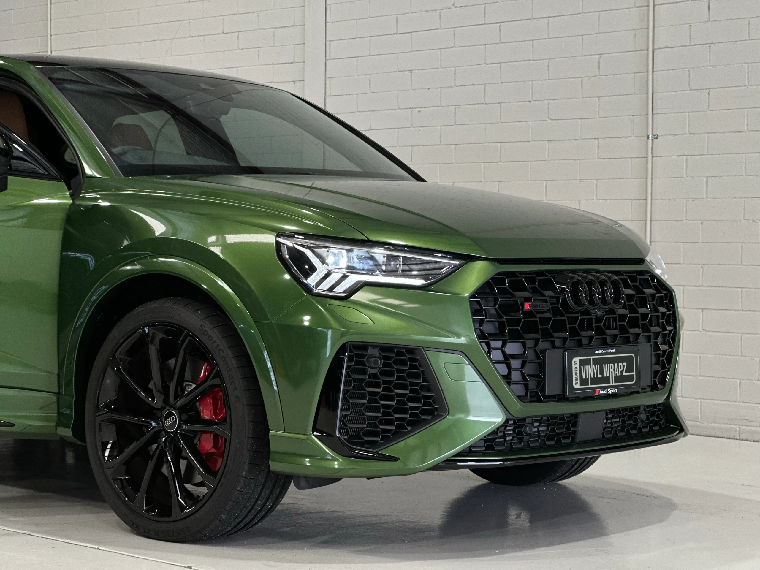 Low front-quarter detail of a green Audi RS Q3 Sportback, showing its wheel, red brake caliper and grille