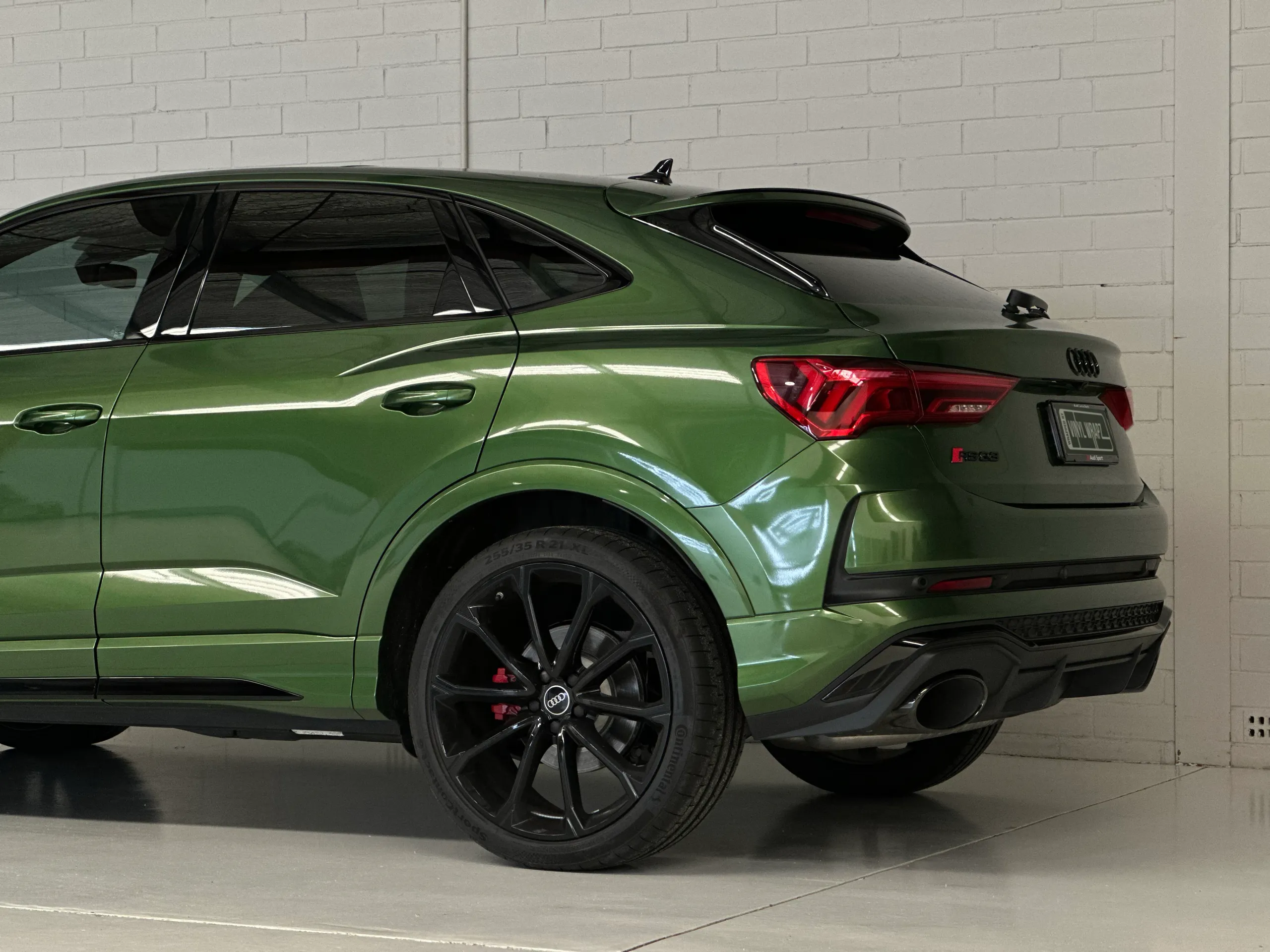 Metallic green Audi RS Q3 Sportback rear quarter and black wheel against a white workshop wall