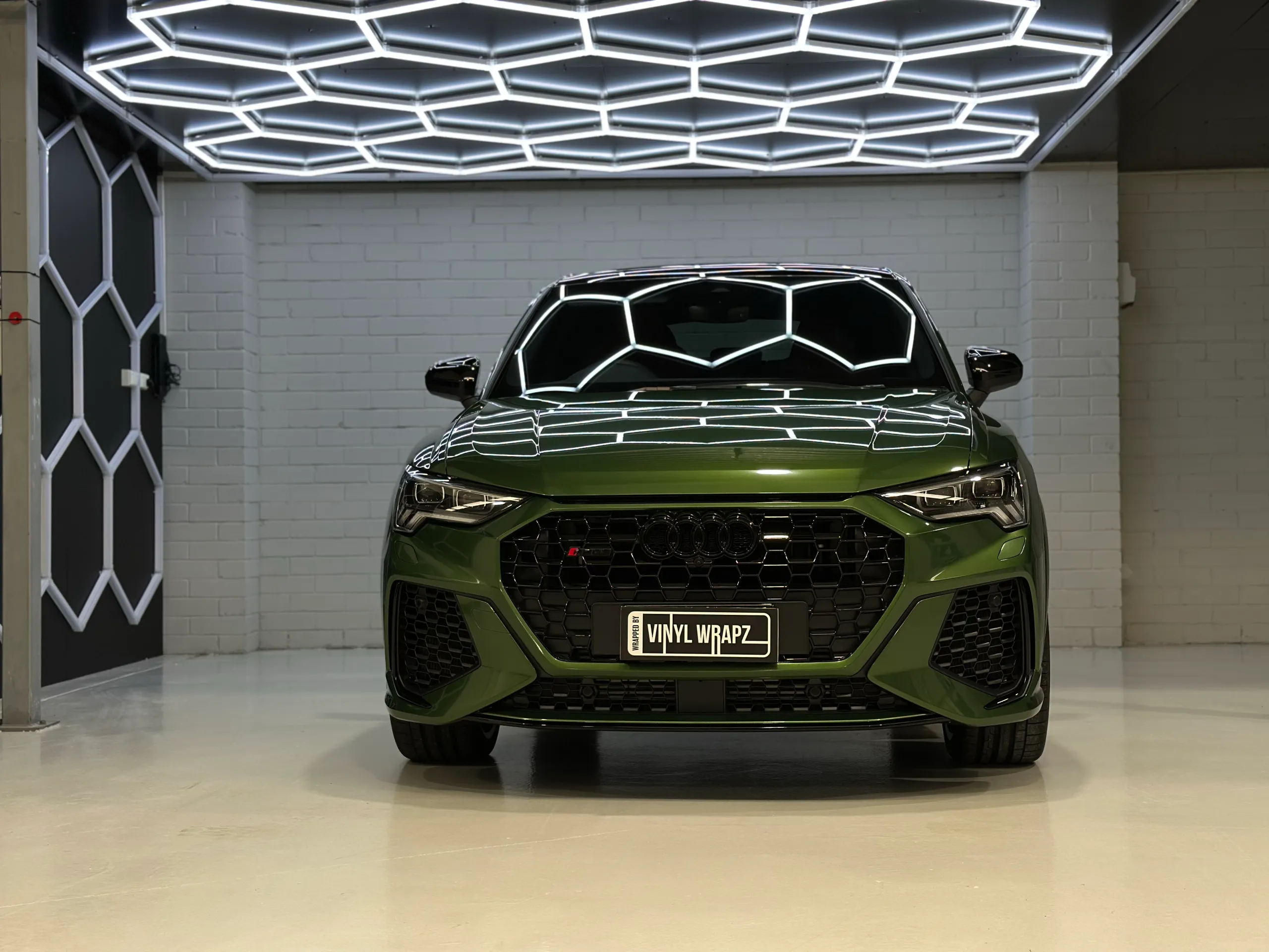 Green Audi RS Q3 Sportback facing the camera beneath a ceiling of hexagonal lights