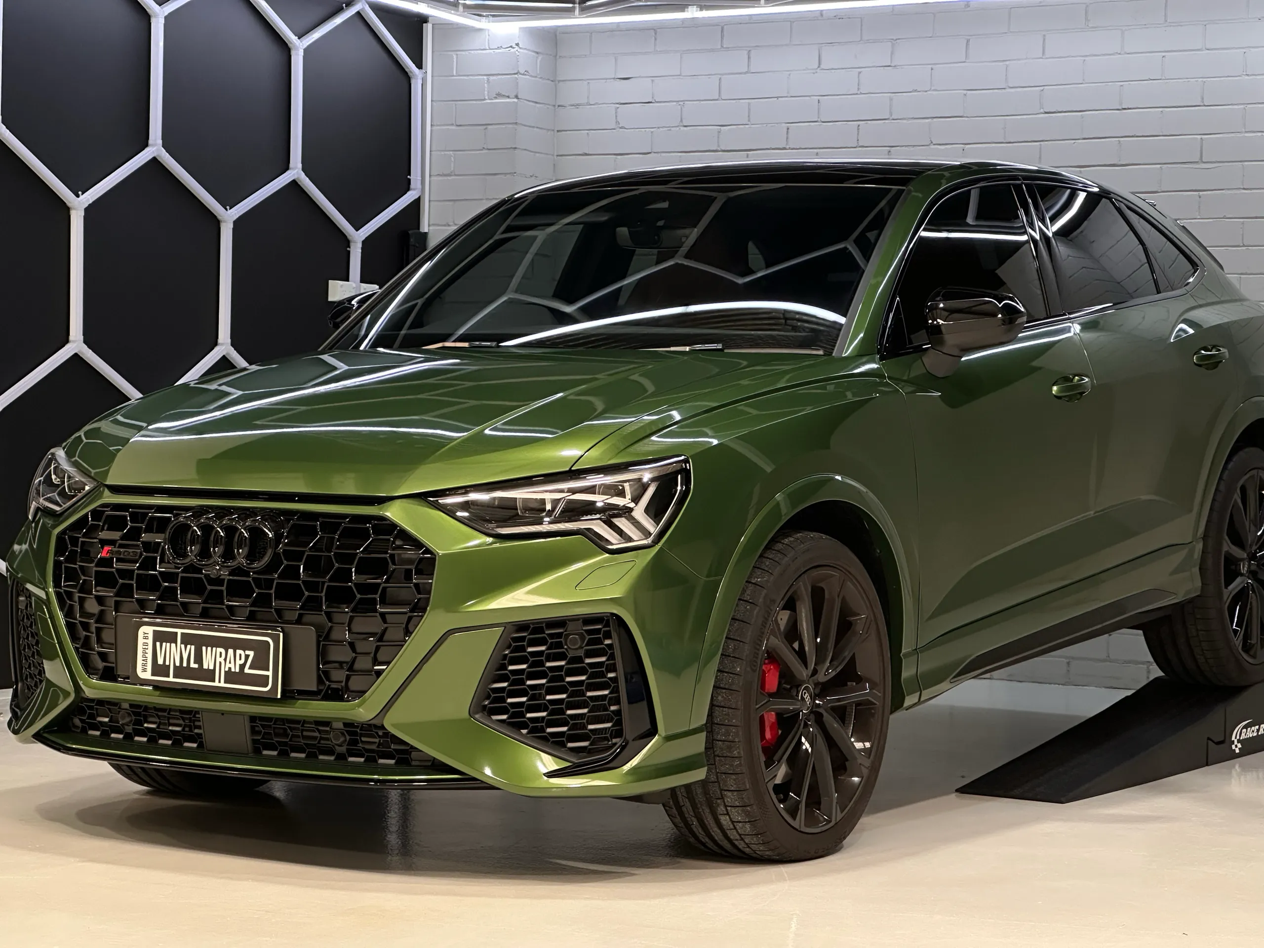 Metallic green Audi RS Q3 Sportback viewed from the front quarter beside a workshop ramp