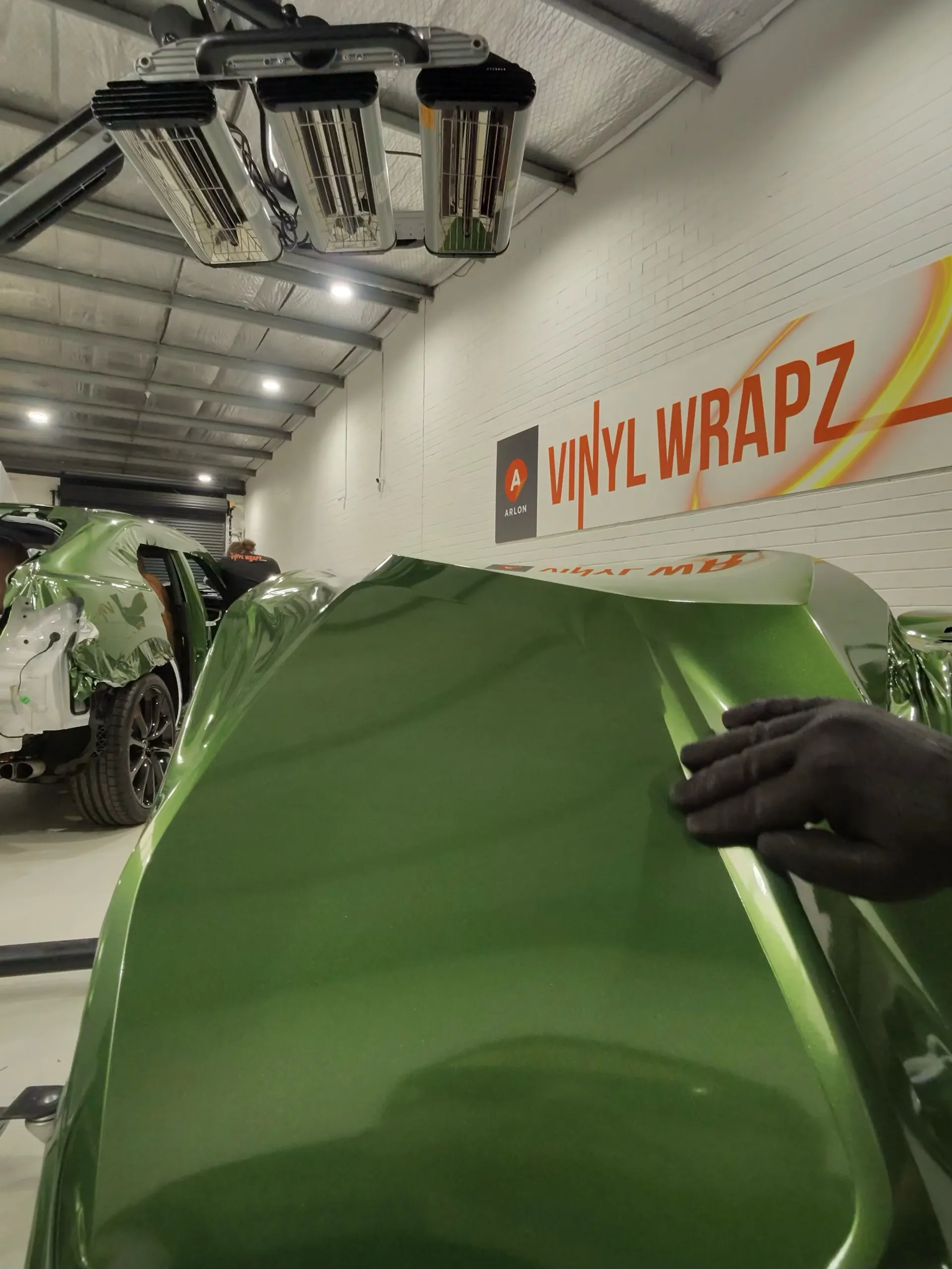Installer's gloved hand smoothing green film over a removed Audi door panel