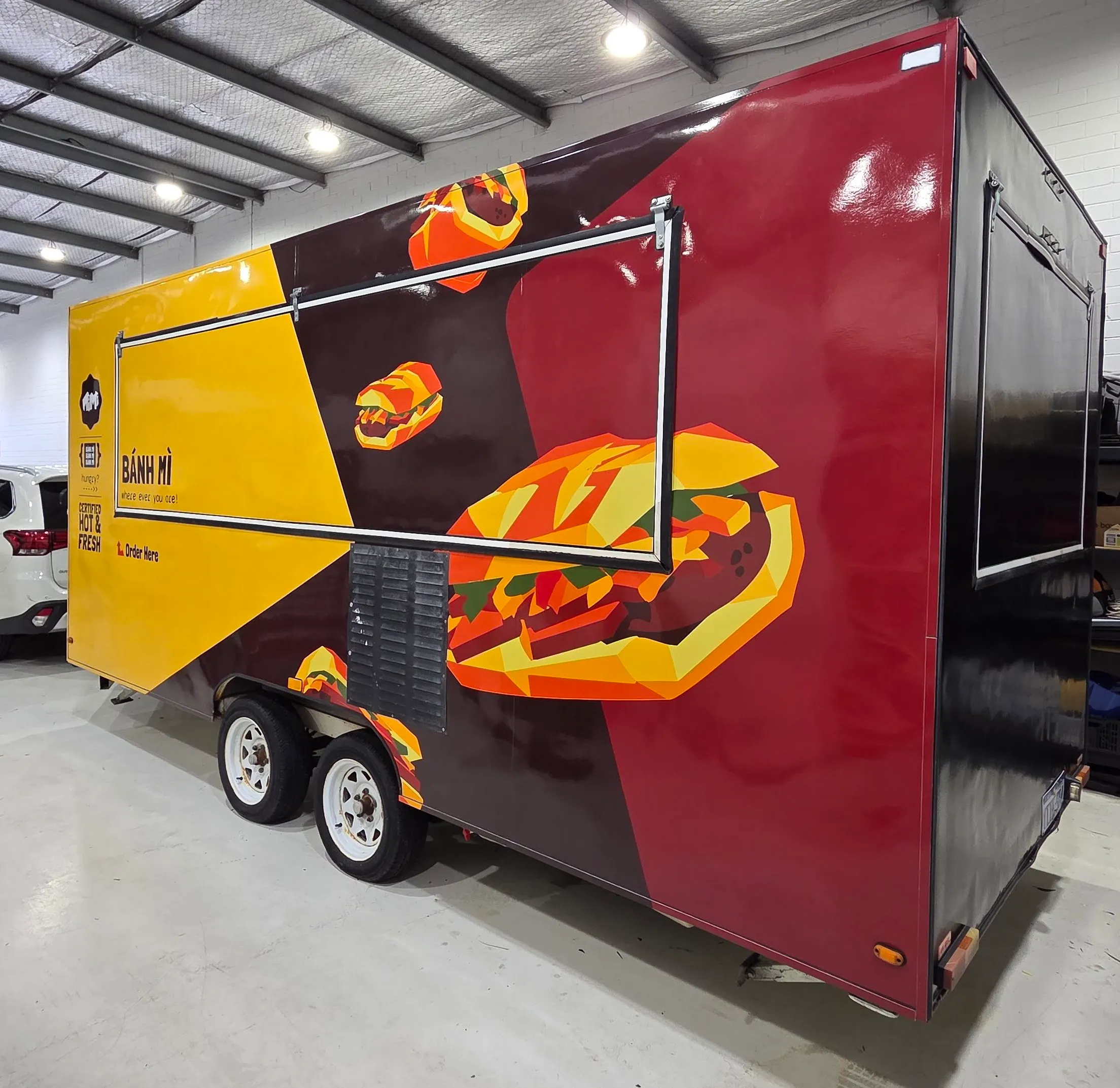 Banh mi food trailer with yellow, burgundy and black graphics and illustrated sandwiches across its closed serving hatch