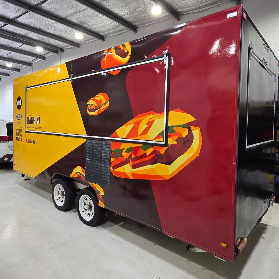 Banh mi food trailer with yellow, burgundy and black graphics and illustrated sandwiches across its closed serving hatch