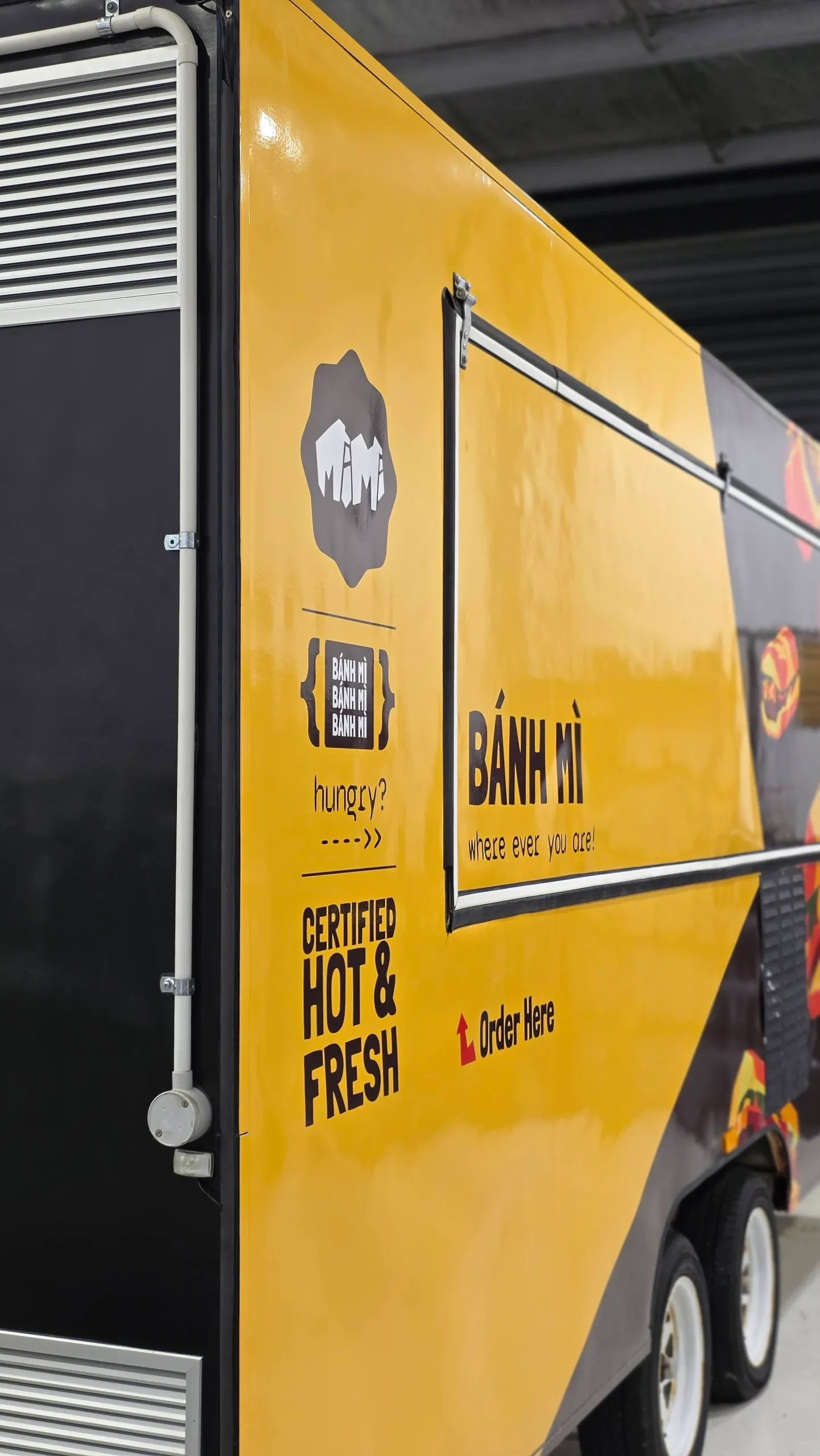 Yellow side panel of a banh mi food trailer, showing the closed serving hatch and order-here lettering