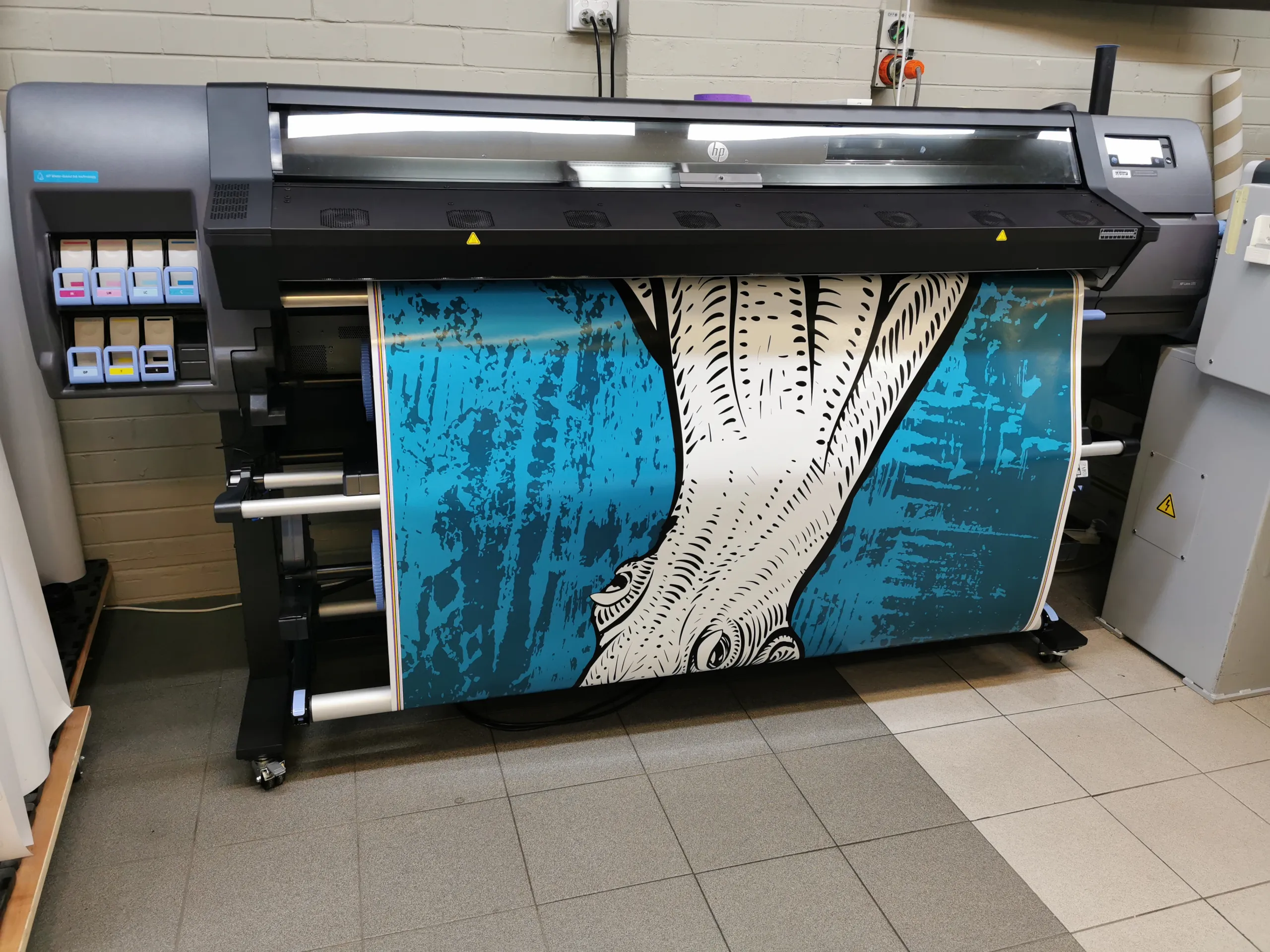 White squid artwork on a blue background emerging from a wide-format printer for a boat wrap